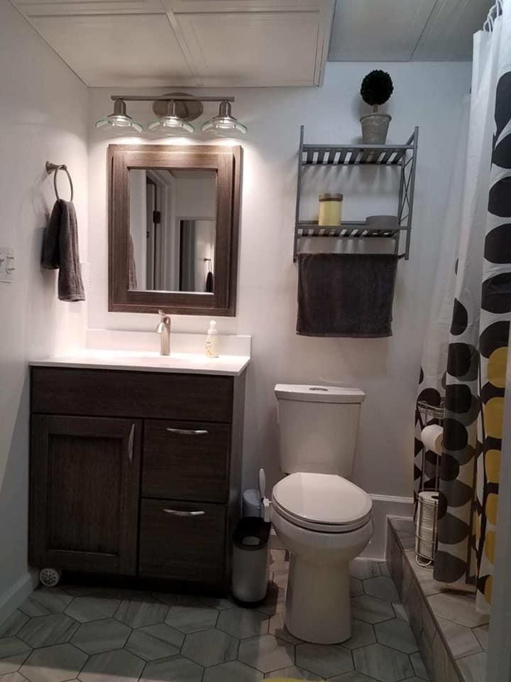 Small bathroom with dark vanity, toilet, mirror, shelf, and patterned shower curtain.