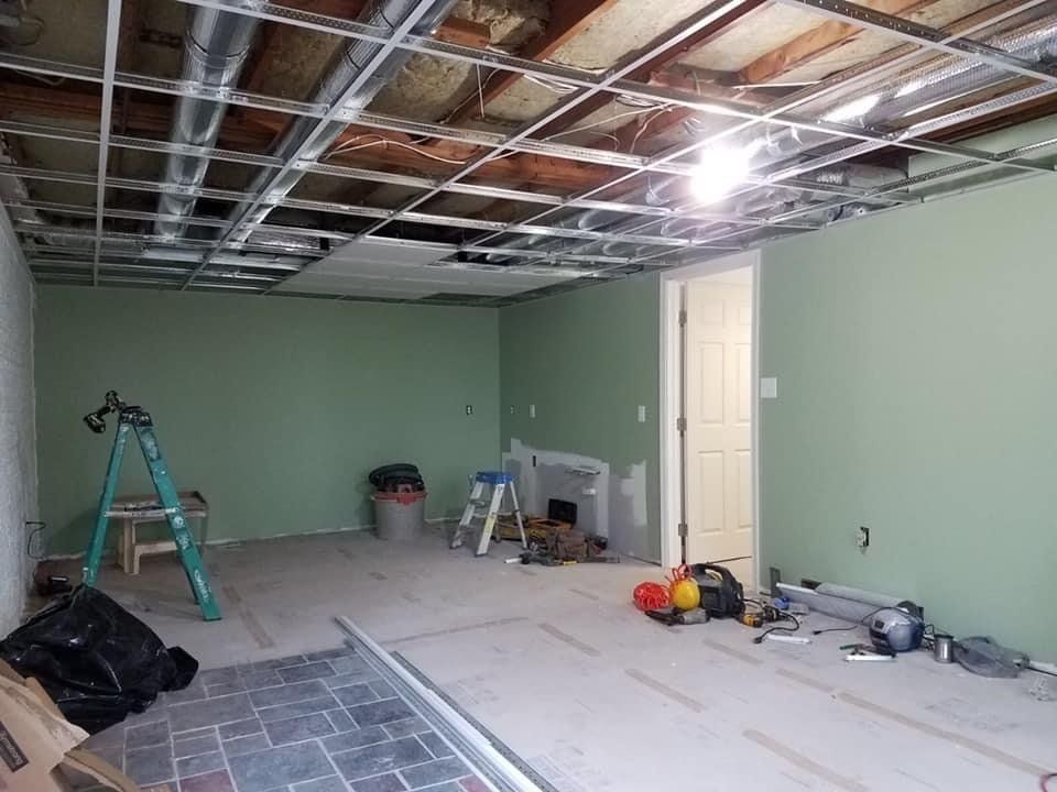 Partially renovated room with exposed ceiling, green walls, ladders, and tools scattered on the floor