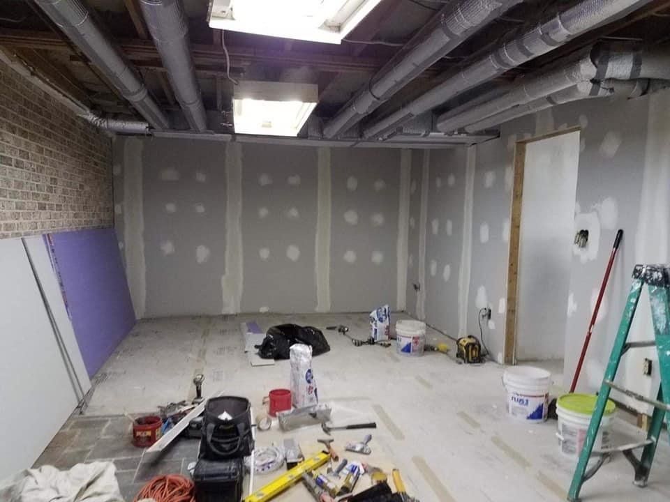 Unfinished basement room with drywall, tools, and a ladder during renovation.