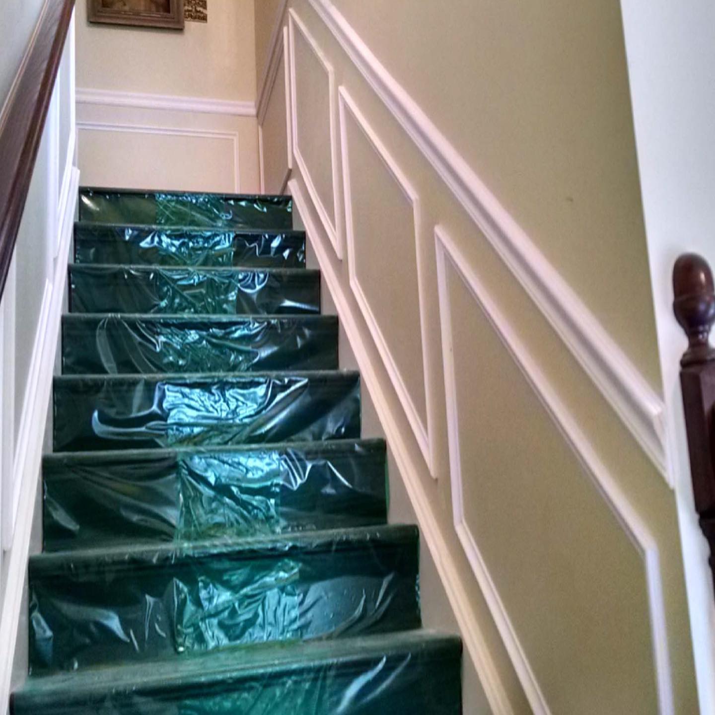 Staircase covered in green plastic sheeting with white banister and beige walls indoors