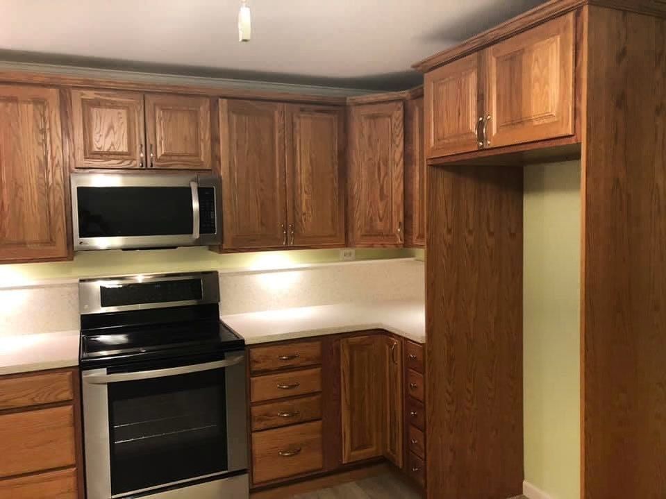 Wooden kitchen with dark appliances, light countertops, and upper cabinets around a corner nook
