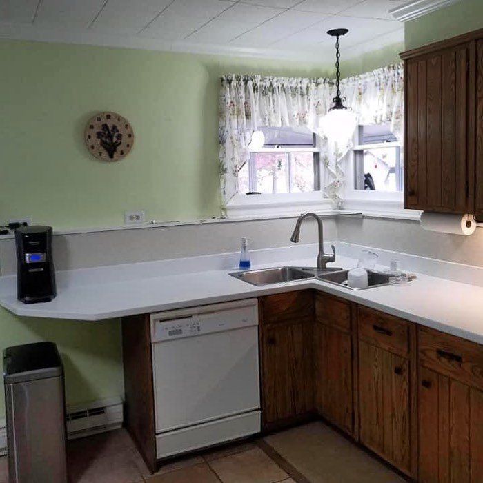 Small kitchen with white countertops, wood cabinets, sink, dishwasher, and a window over the counter.