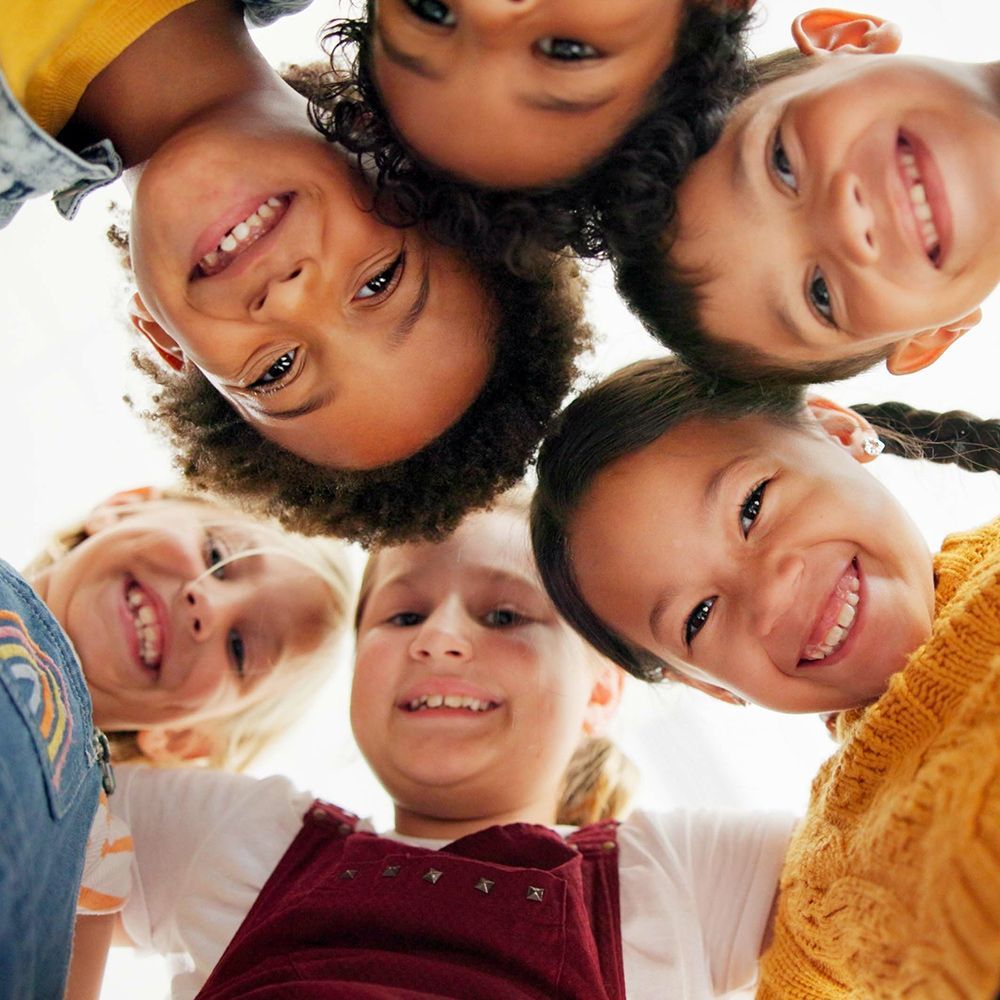 Group of diverse children smiling, looking down in a circle.