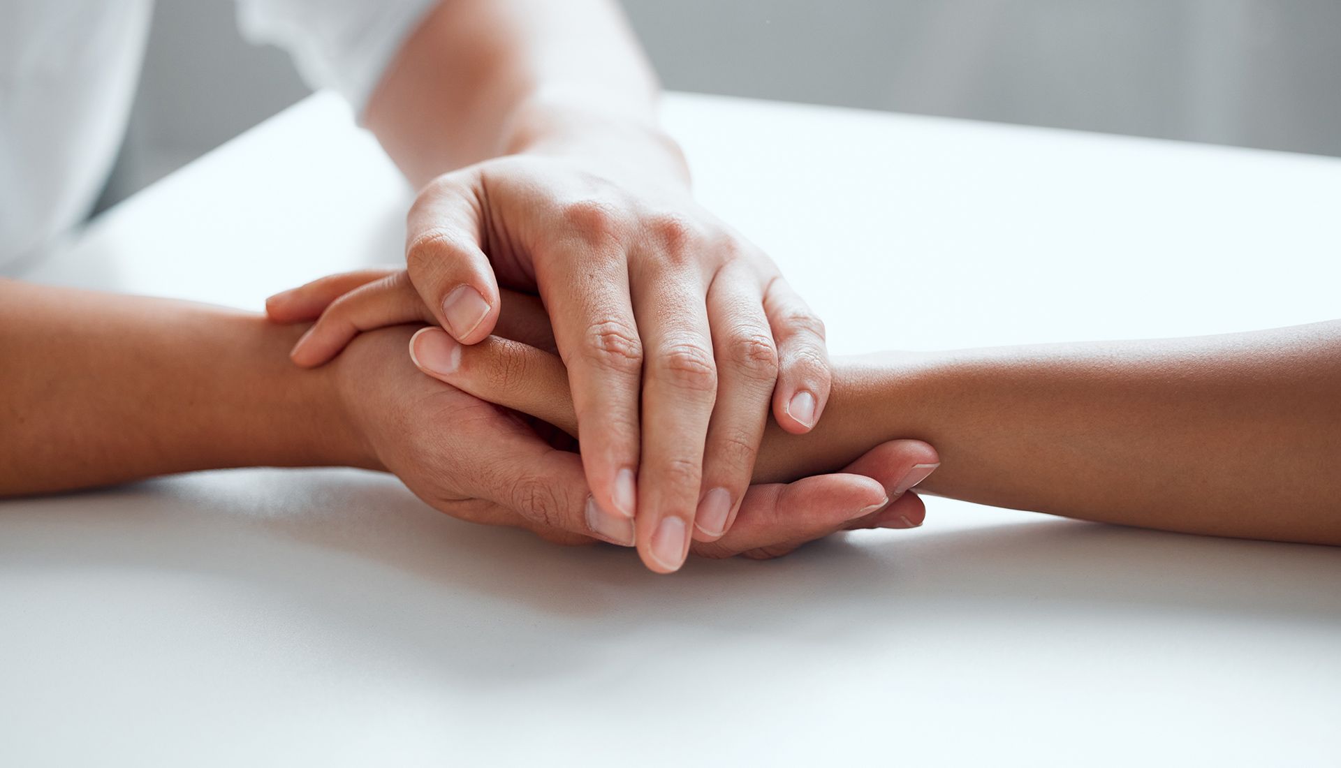 Hands clasped together on a white surface, offering comfort and support.