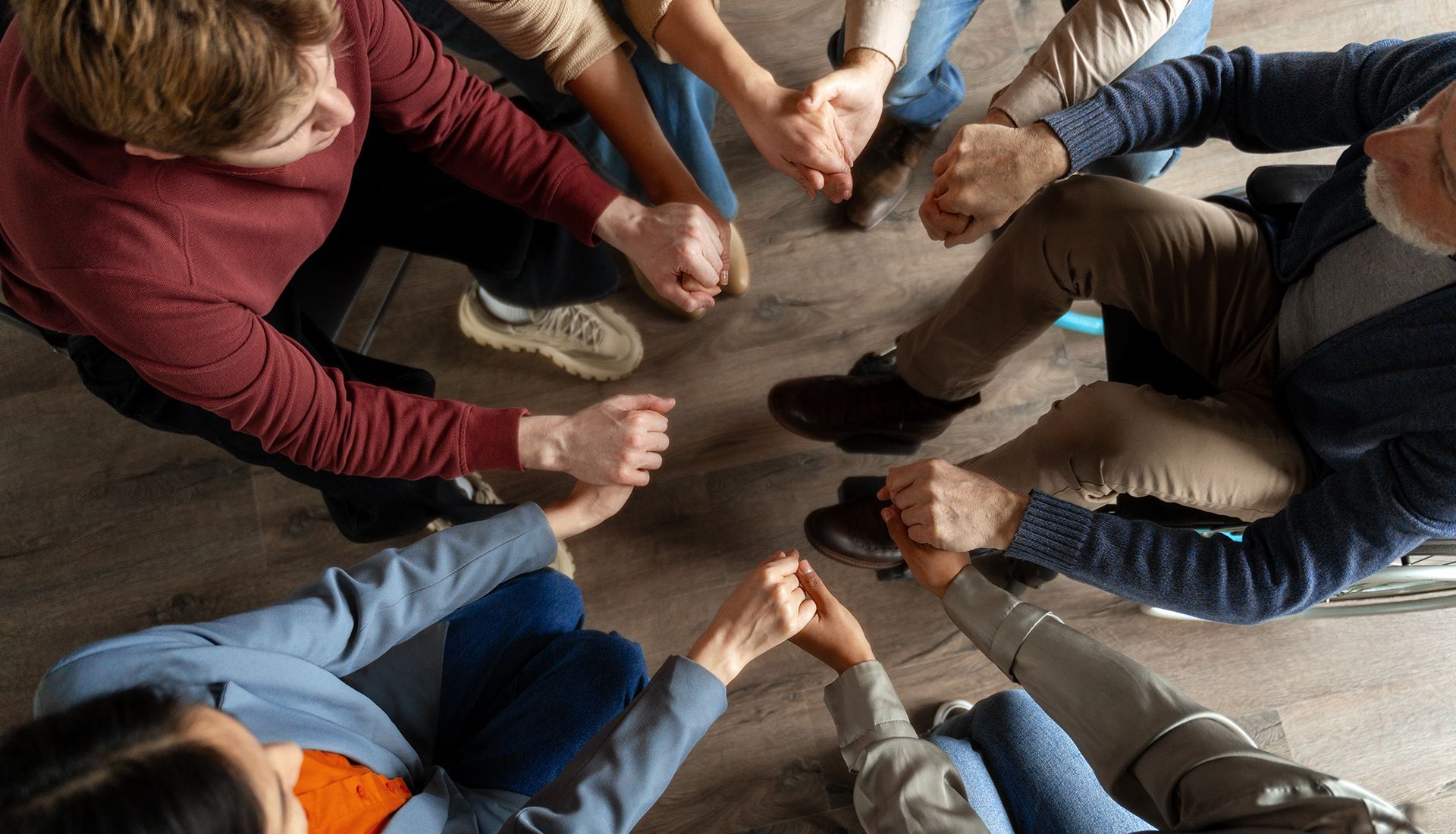 People in a circle holding hands, seen from above. Focus on their joined hands, fostering community.