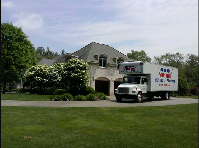 Moving truck parked in front of a large house with a manicured lawn and trees.