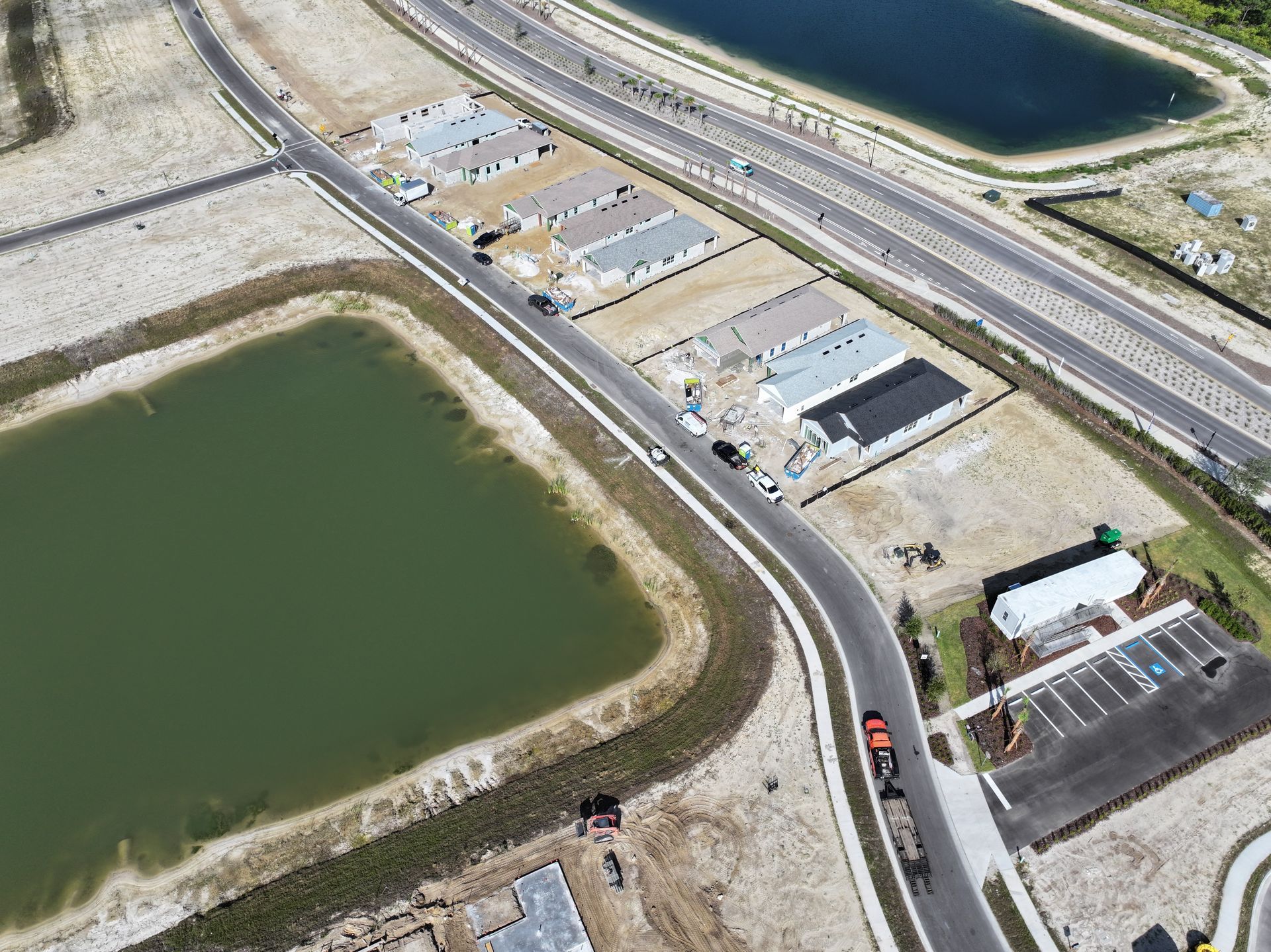 Aerial view of industrial buildings beside green ponds, roads, and a canal with a small orange vehicle.