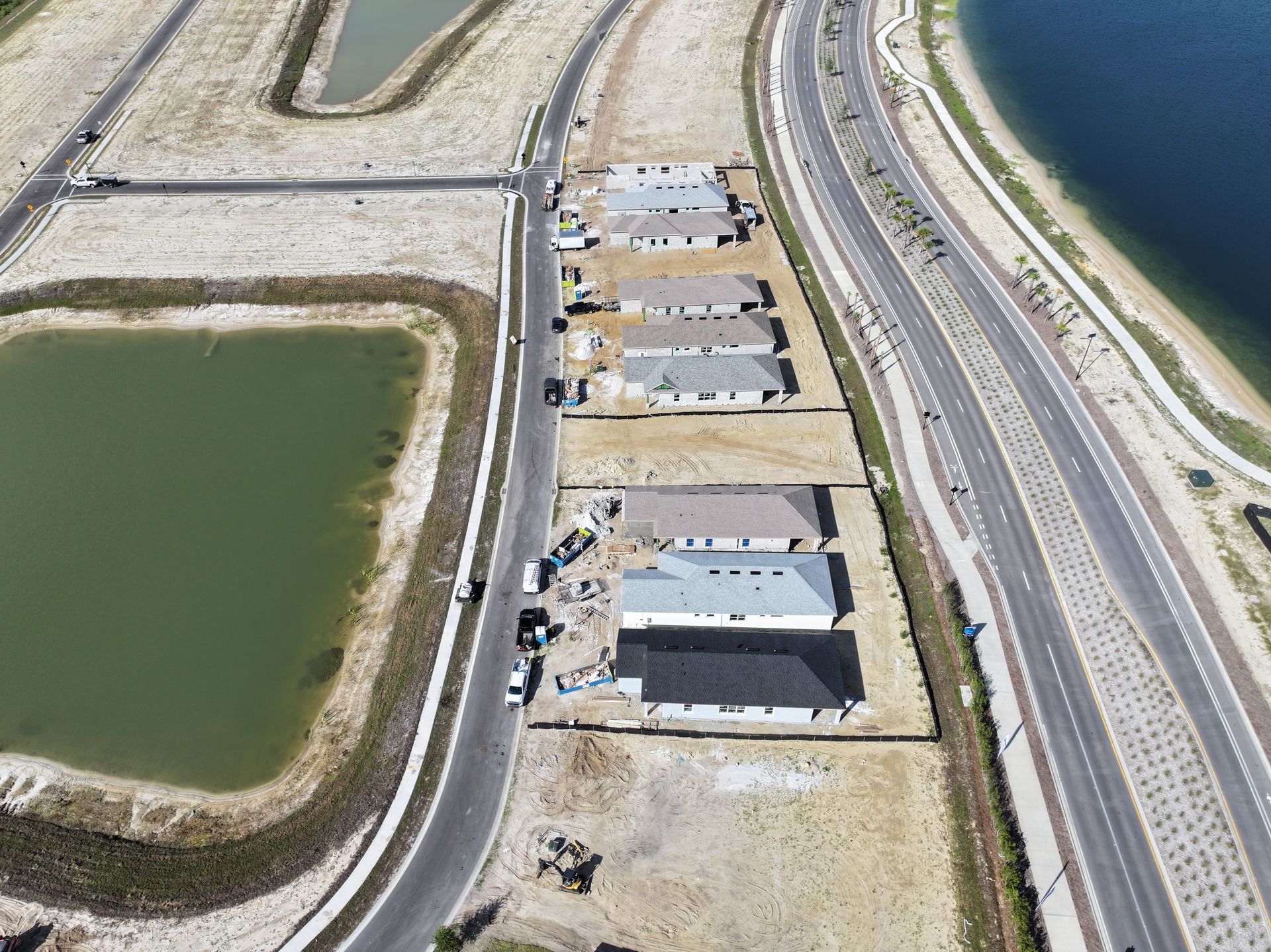 Aerial view of coastal road, small buildings, and green water basins beside a shoreline.