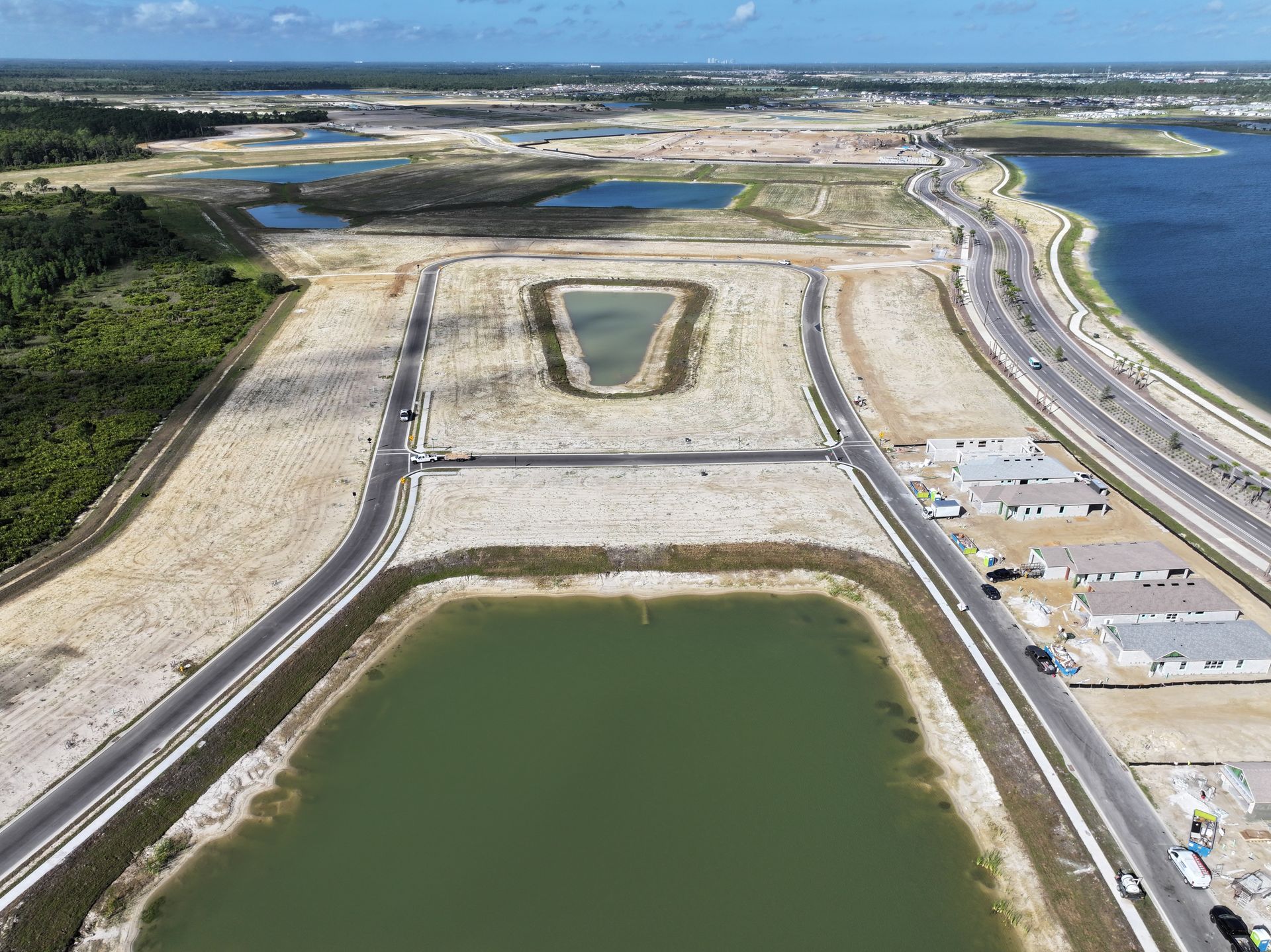 Aerial view of a coastal landscape with large ponds, roads, and seawater beside a shoreline.