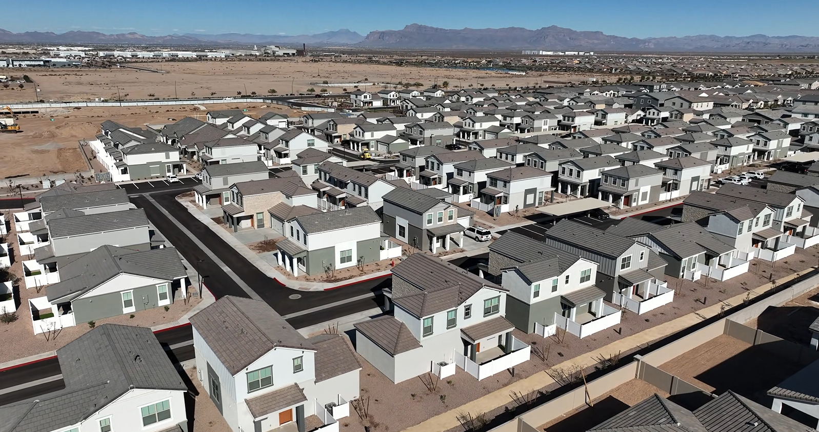 Aerial view of a suburban housing development with rows of white houses and distant mountains under a clear sky