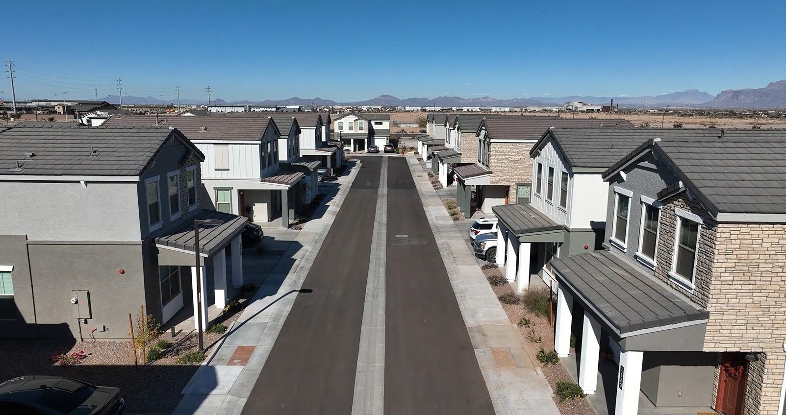 Aerial view of a quiet suburban street with houses on both sides under a clear blue sky.
