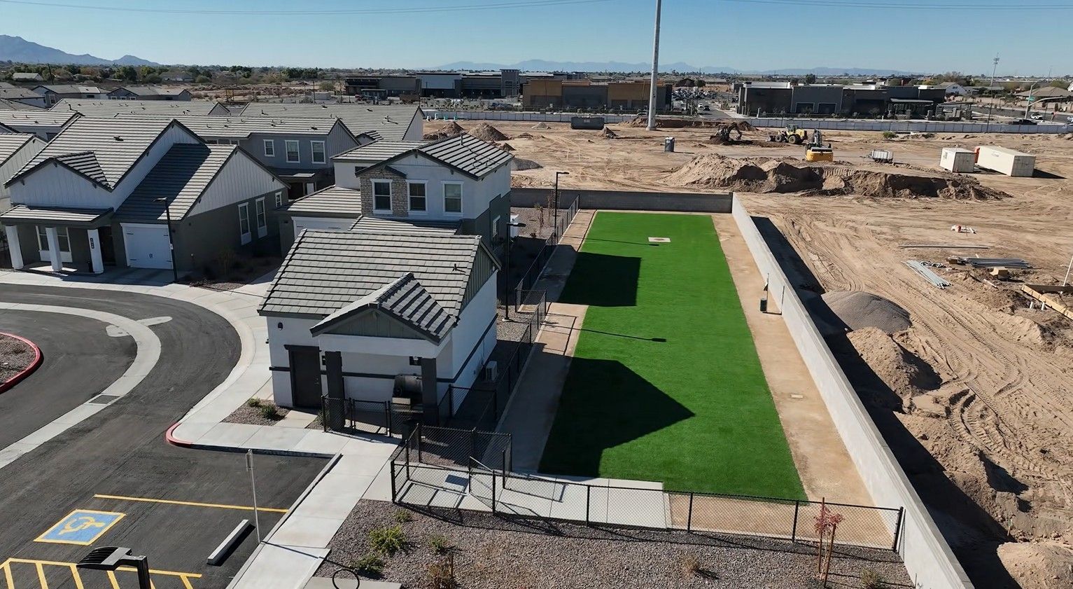 Aerial view of new suburban homes beside a bright green lawn and surrounding construction site.
