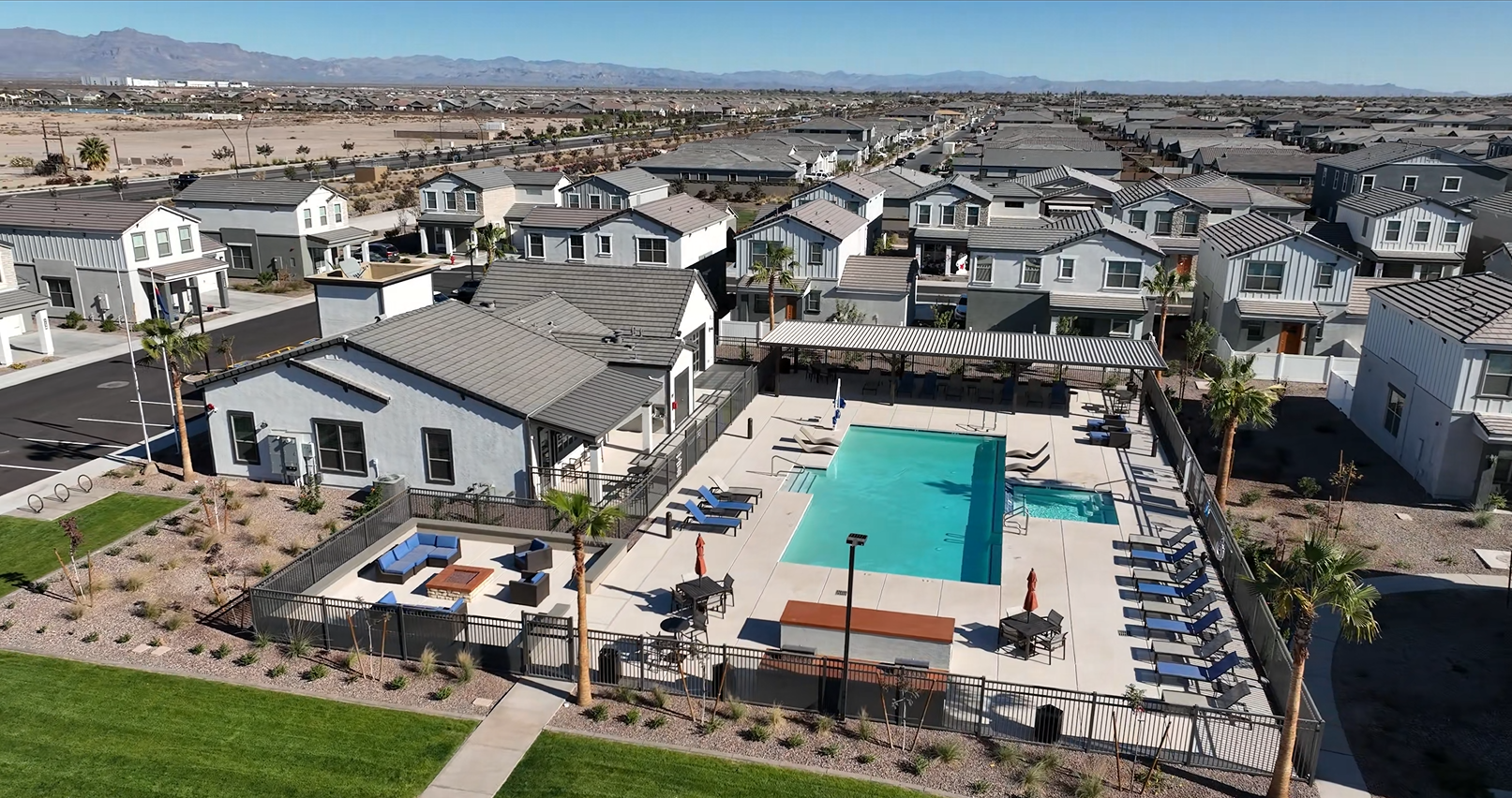 Aerial view of a residential complex with a turquoise pool, lounge chairs, and desert mountains in the background