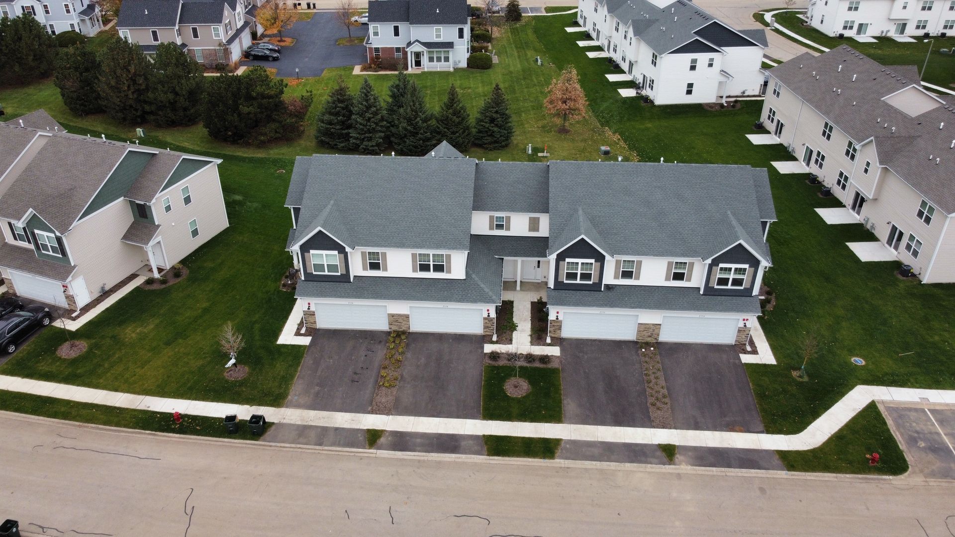 Aerial view of two gray suburban houses with driveways and front lawns along a residential street.
