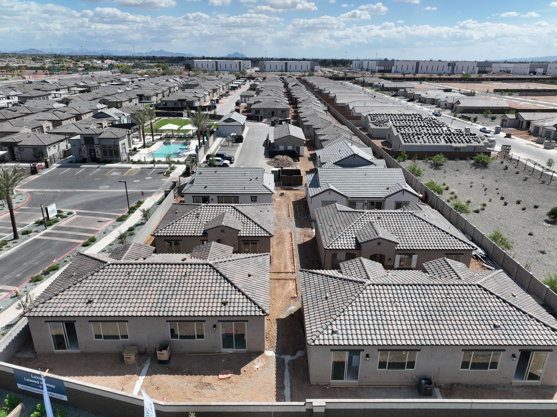 Aerial view of a suburban housing development with rows of beige homes and tiled roofs under a partly cloudy sky
