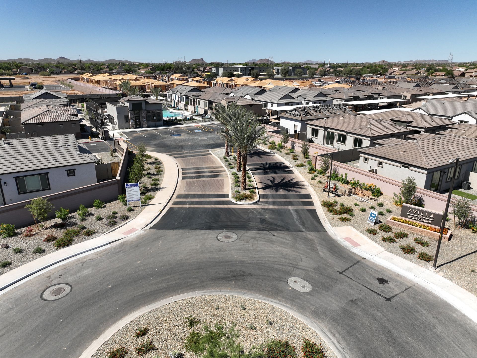 Suburban neighborhood street with a landscaped roundabout and rows of houses under a clear blue sky