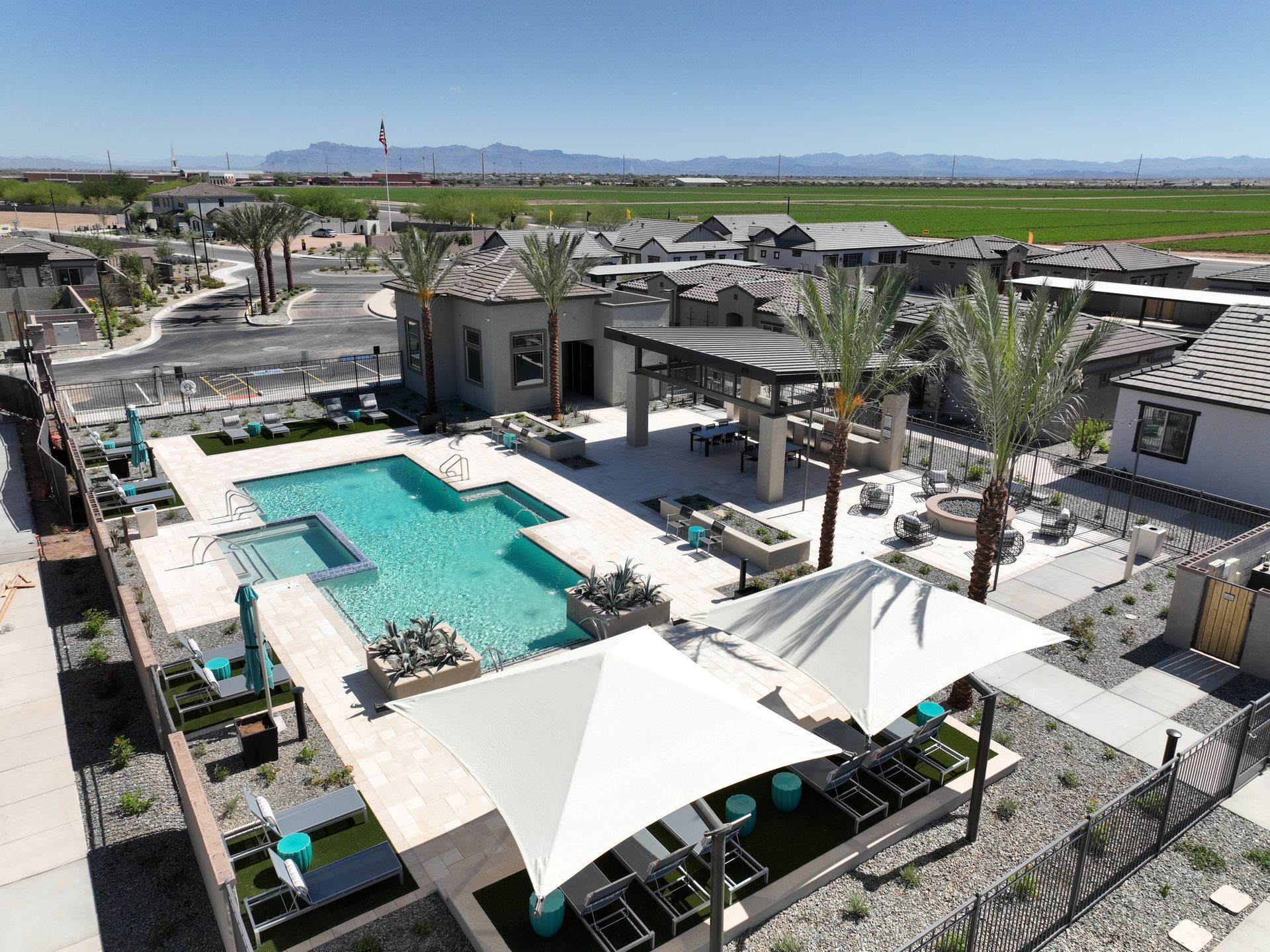 Aerial view of a modern poolside resort with turquoise water, white umbrellas, and palm trees.