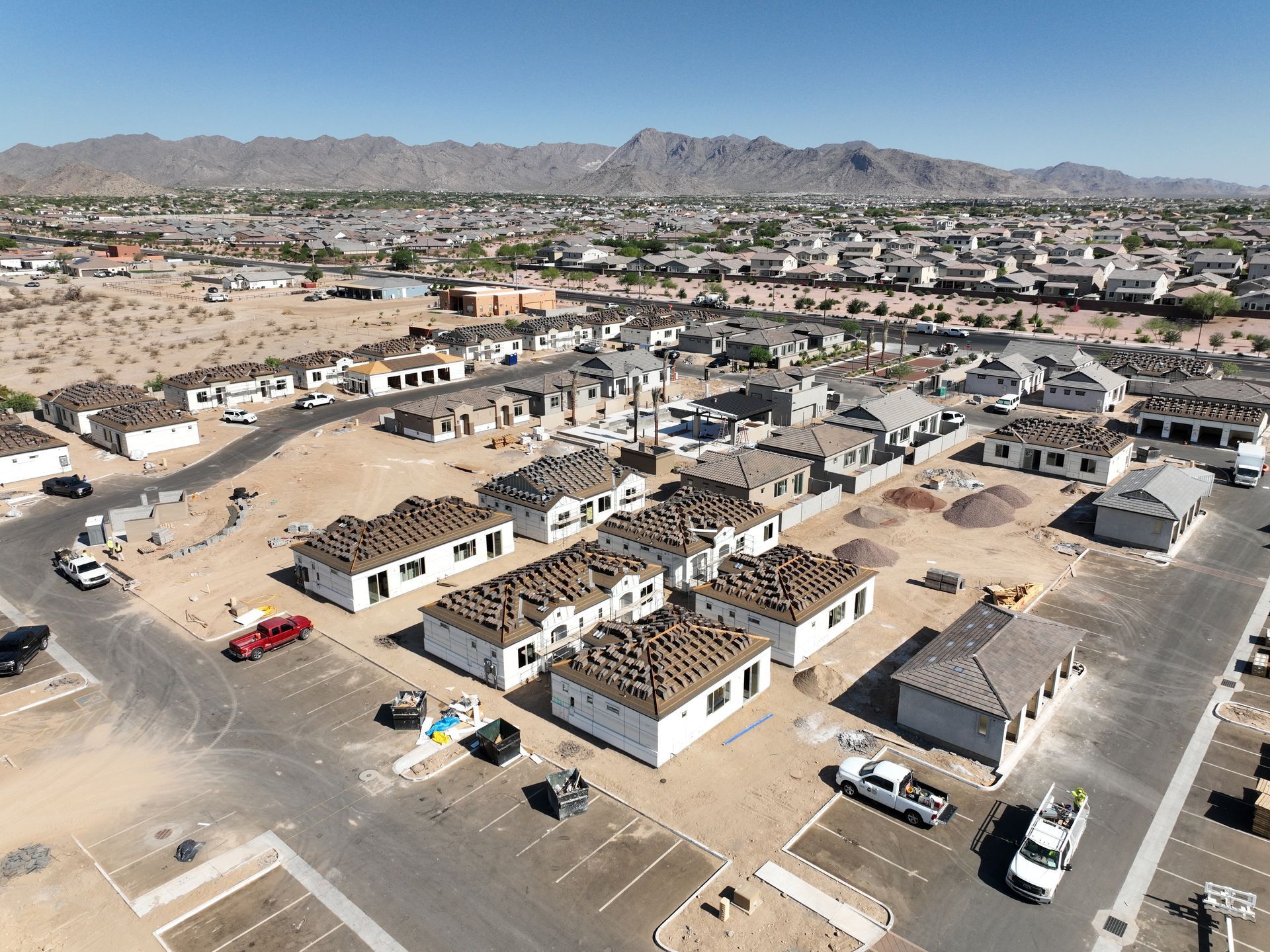 Construction site with concrete foundations and framing in a dusty residential neighborhood under a clear sky