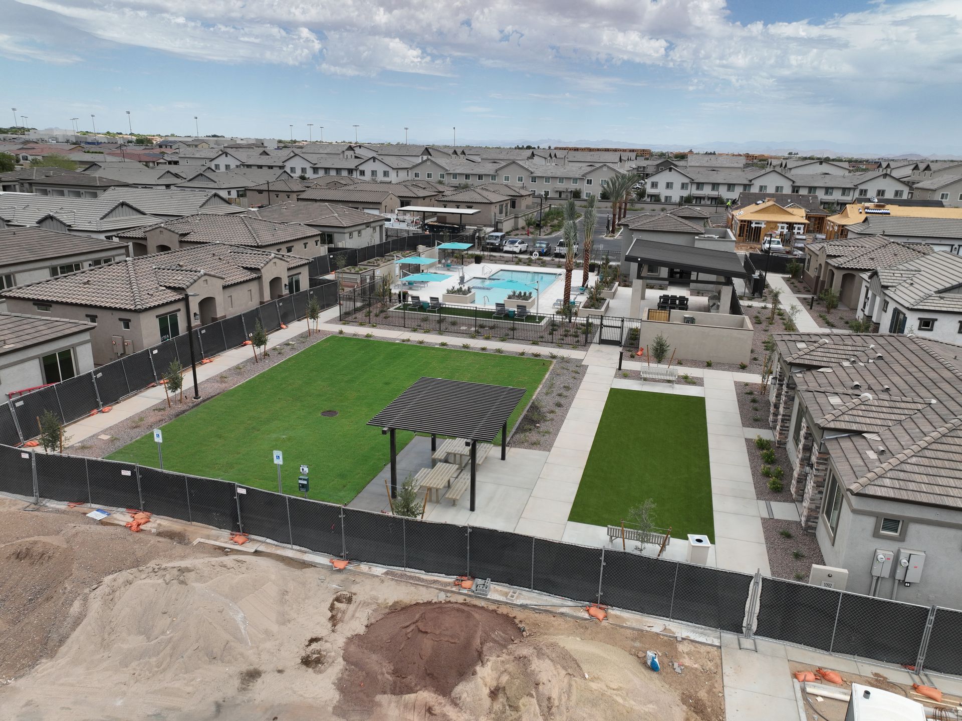 Aerial view of a suburban street with new homes, palm trees, and landscaped medians under a cloudy sky