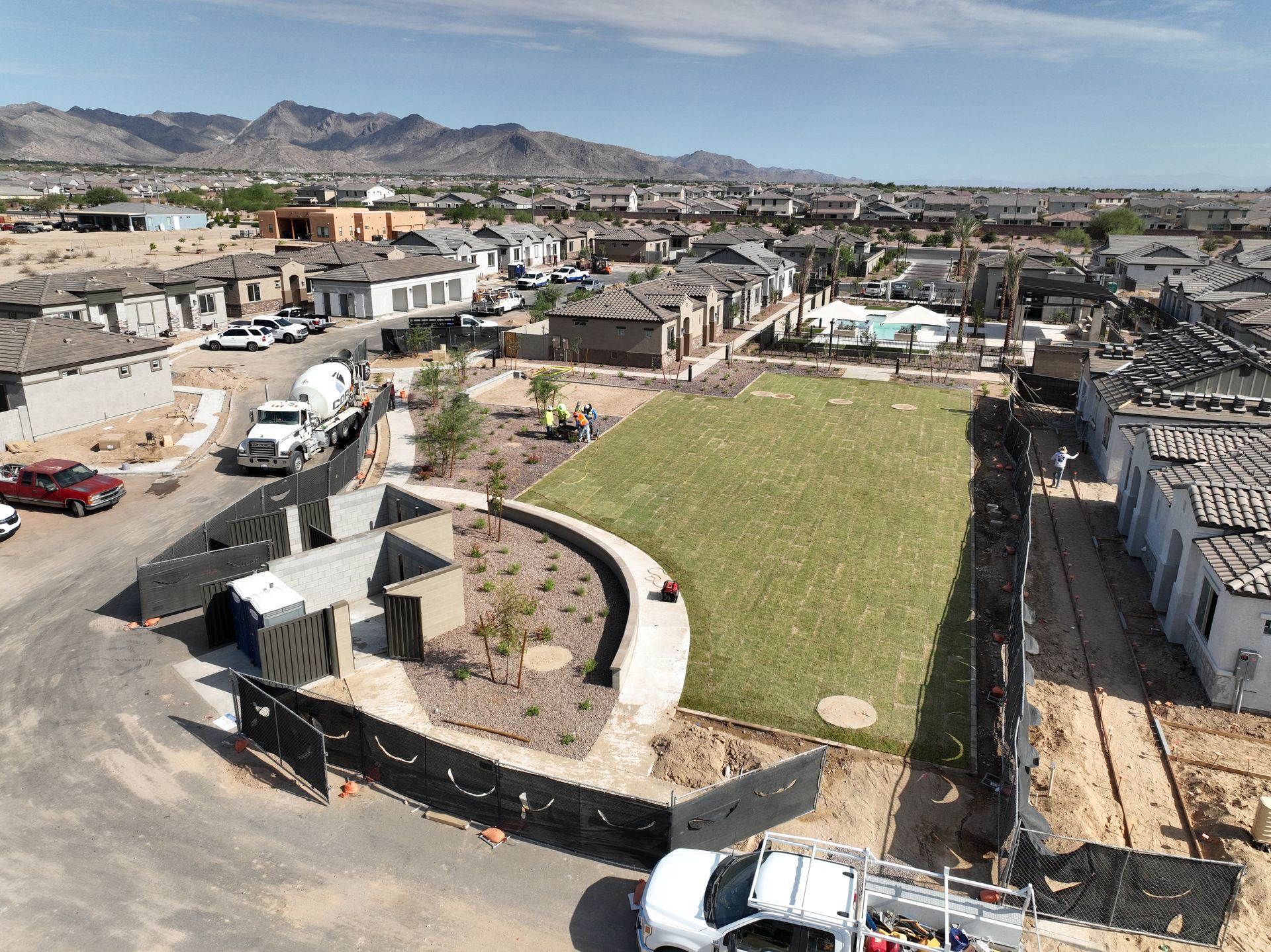 Aerial view of a residential neighborhood with roads, houses, a grassy lot, and mountains in the distance