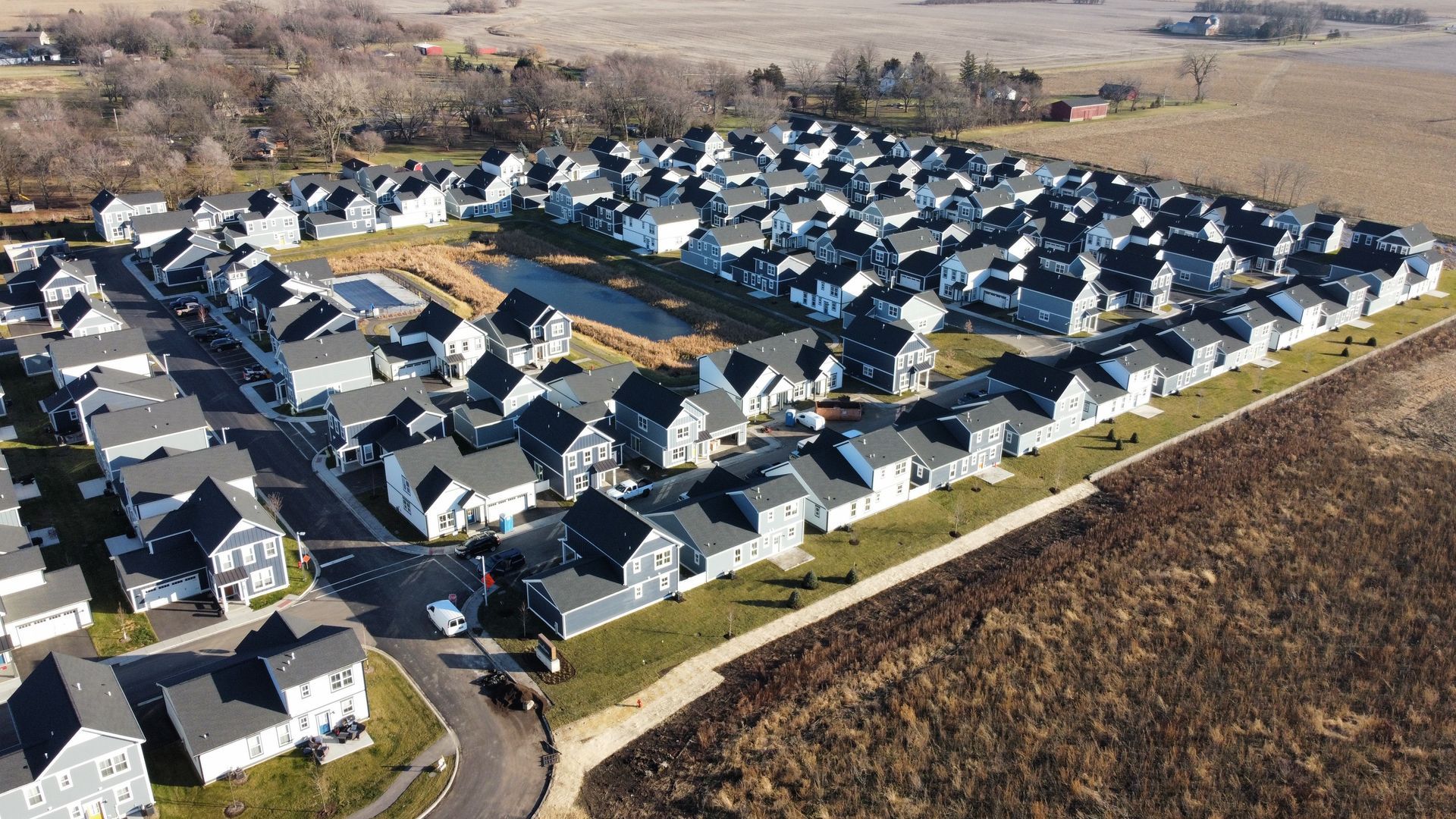 Aerial view of a suburban neighborhood with rows of houses beside open fields on a sunny day
