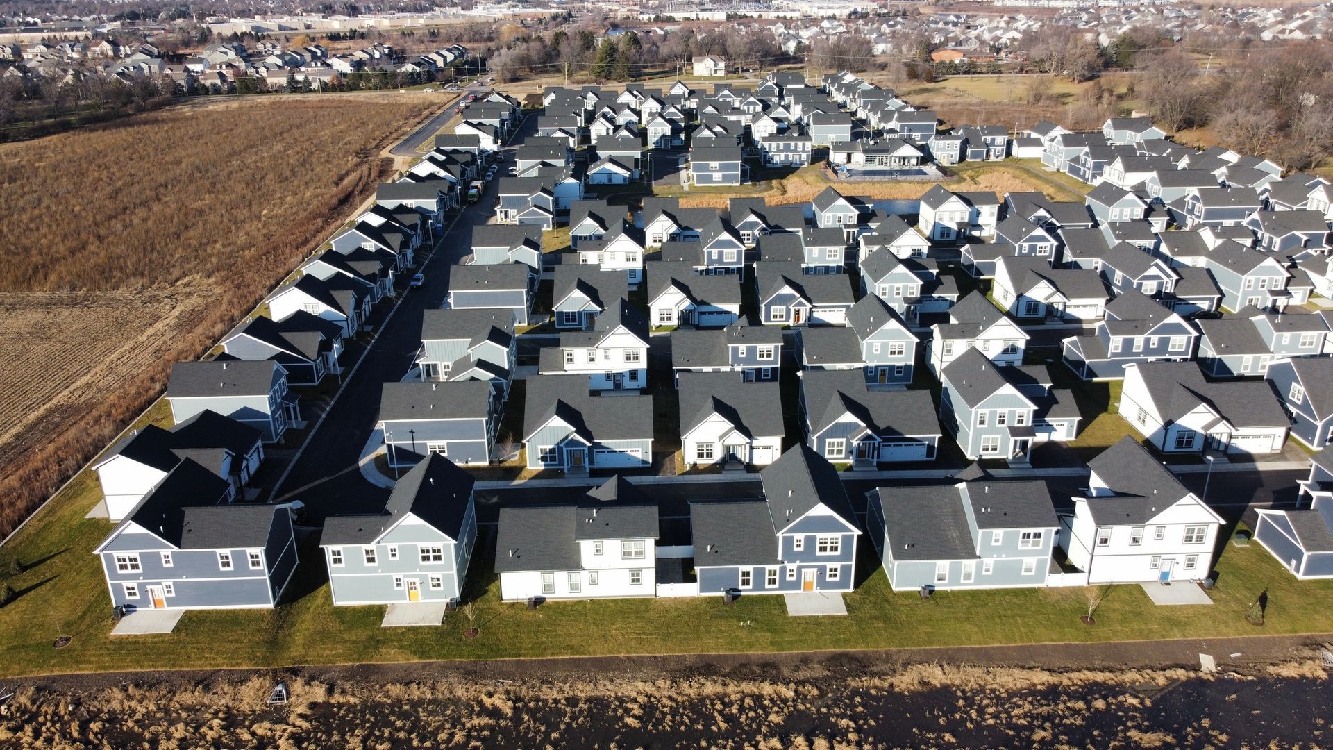 Aerial view of a dense suburban neighborhood with rows of gray-roofed houses beside open fields