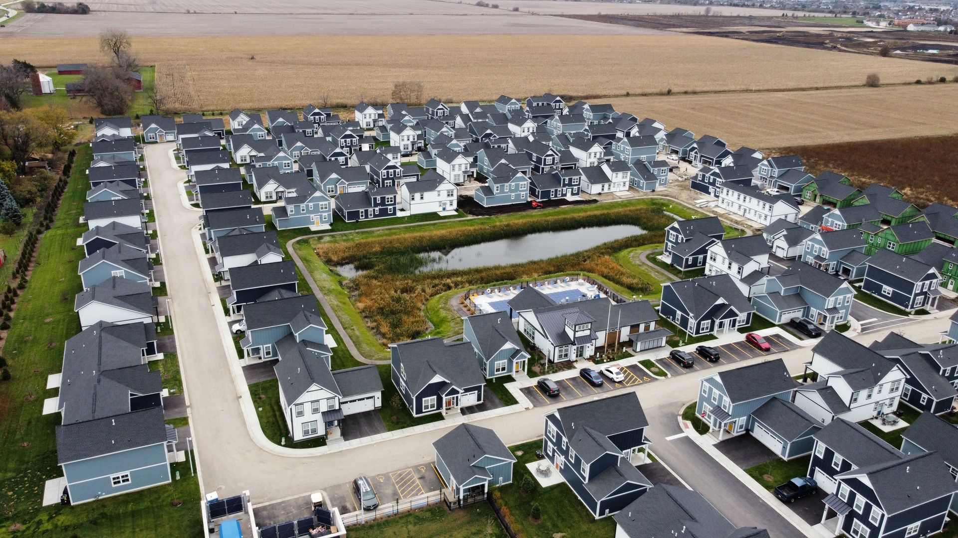 Aerial view of a suburban housing development with rows of gray-roofed houses and surrounding farmland