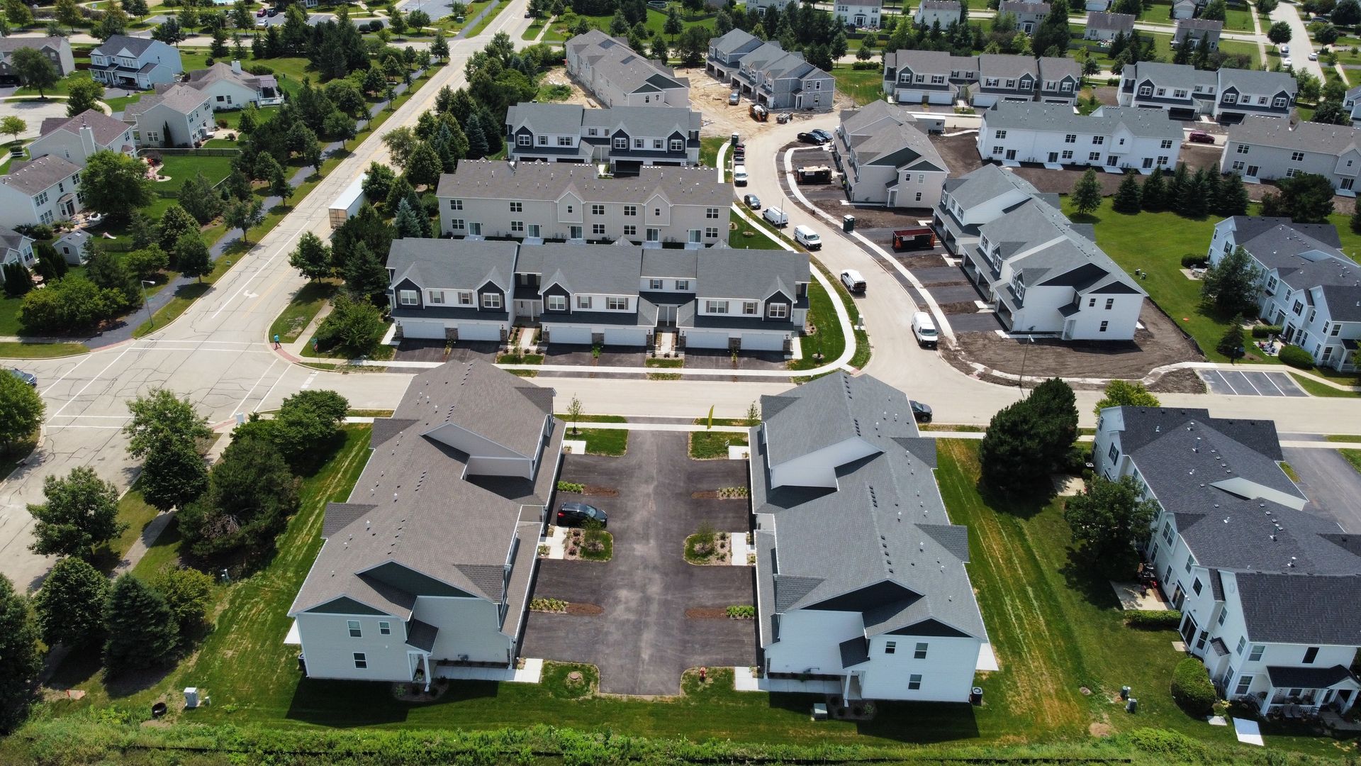 Aerial view of a white duplex with gray roof, front porches, driveways, and paved parking area