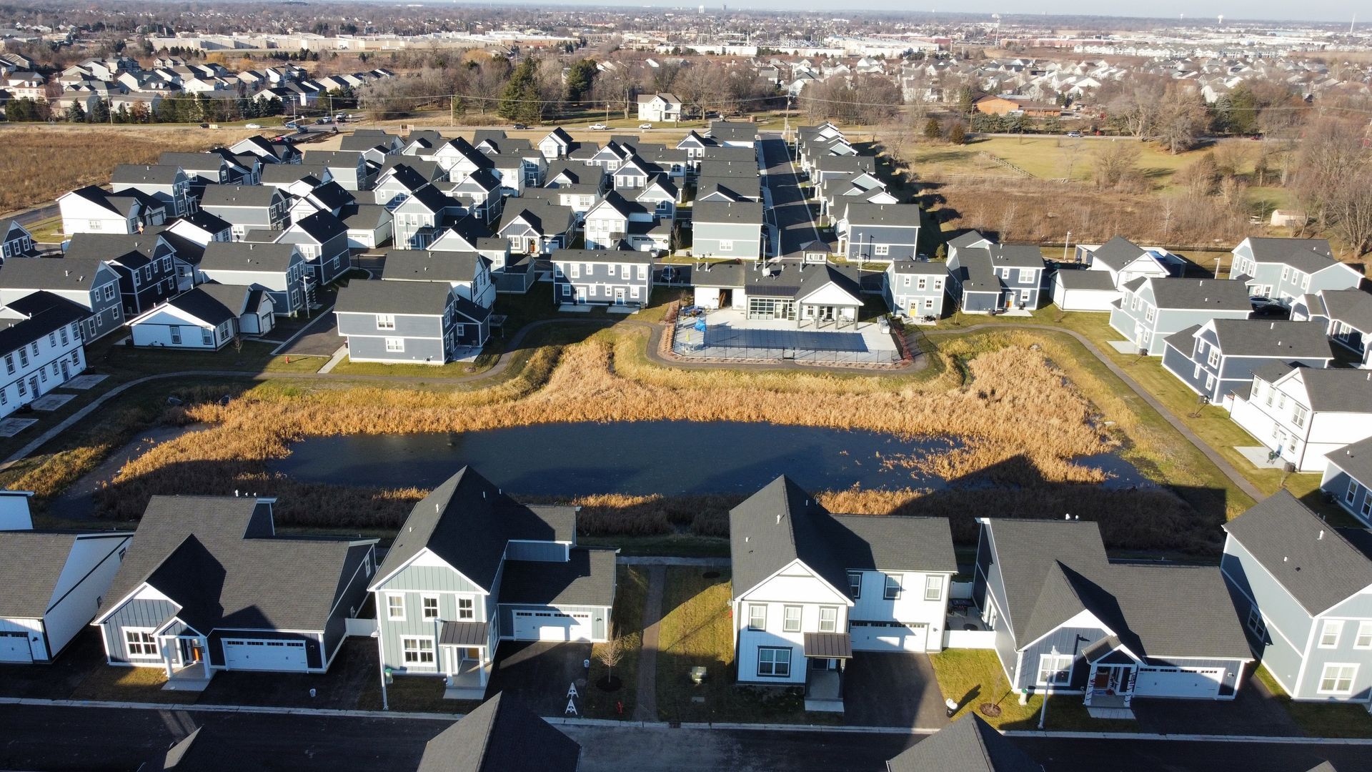 Aerial view of a suburban neighborhood with rows of gray houses around a central grassy lot.