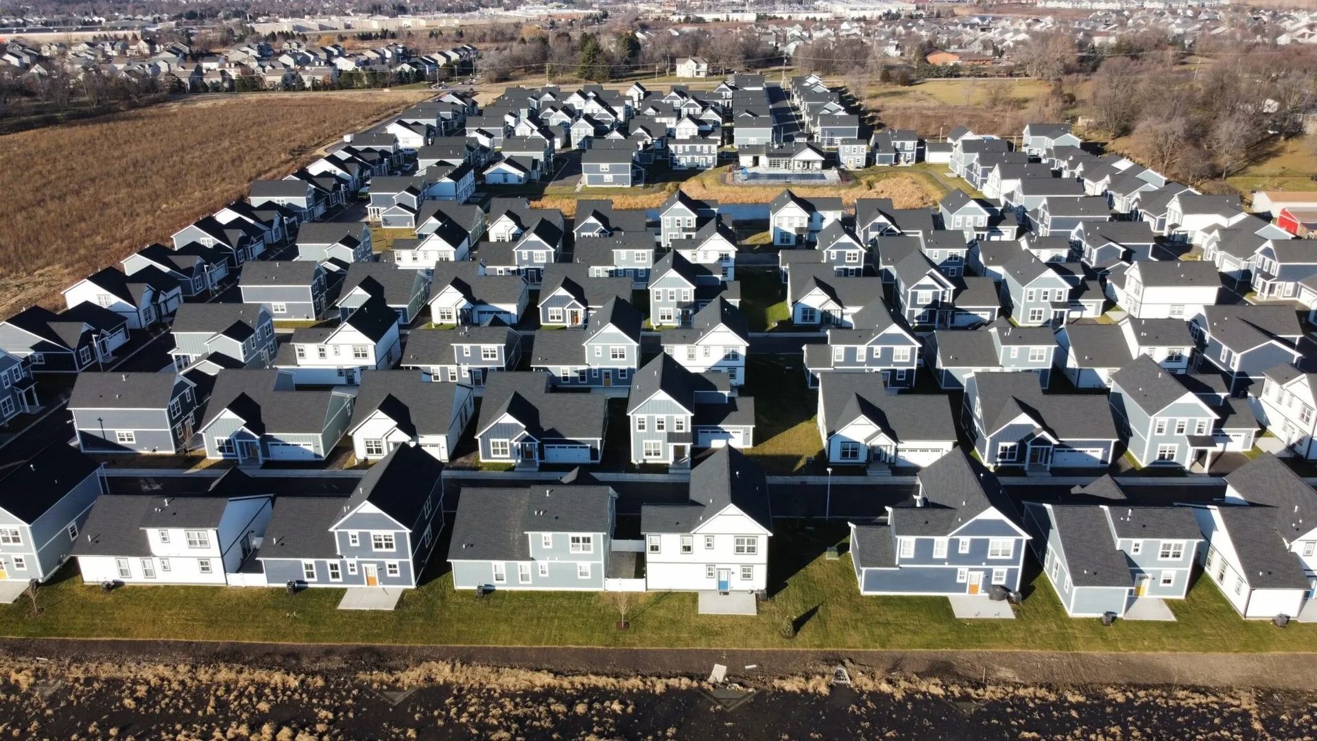 Aerial view of a dense suburban neighborhood with rows of gray-roofed houses and leafless trees