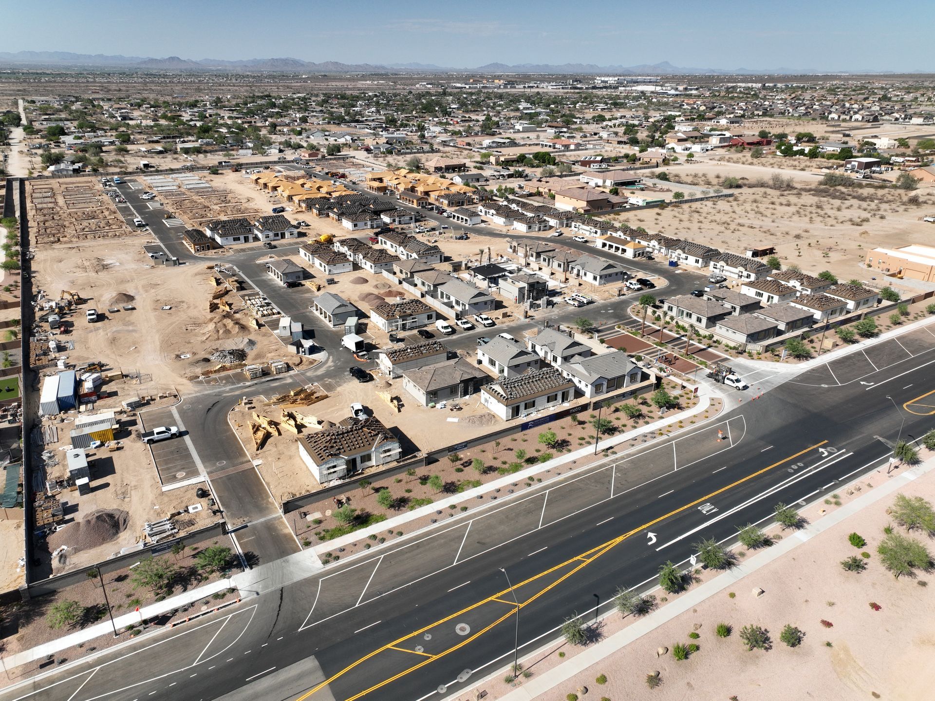 Aerial view of a suburban neighborhood beside a wide road, with mountains in the distance.