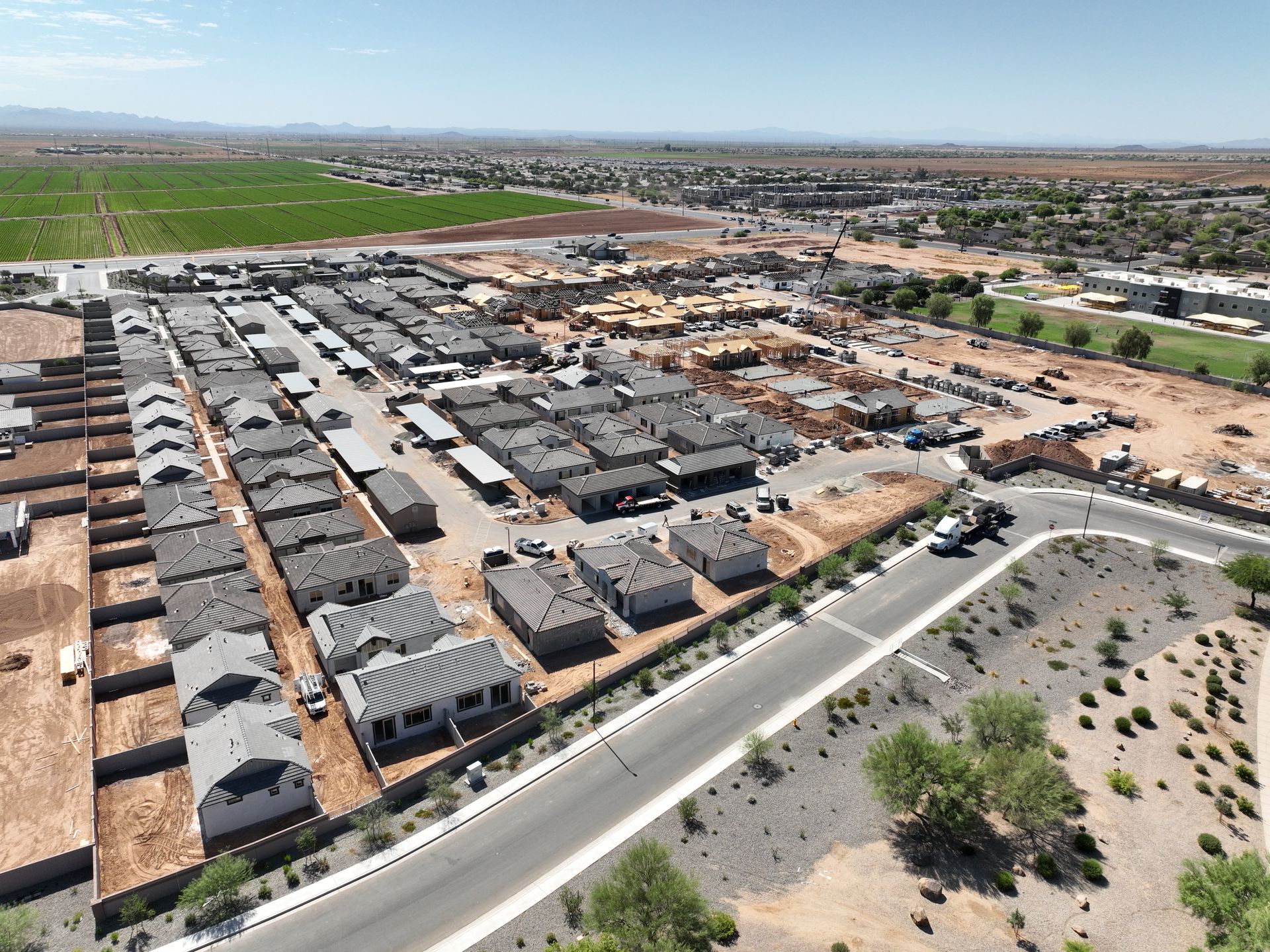 Aerial view of a large housing development with rows of homes, roads, and open green fields nearby