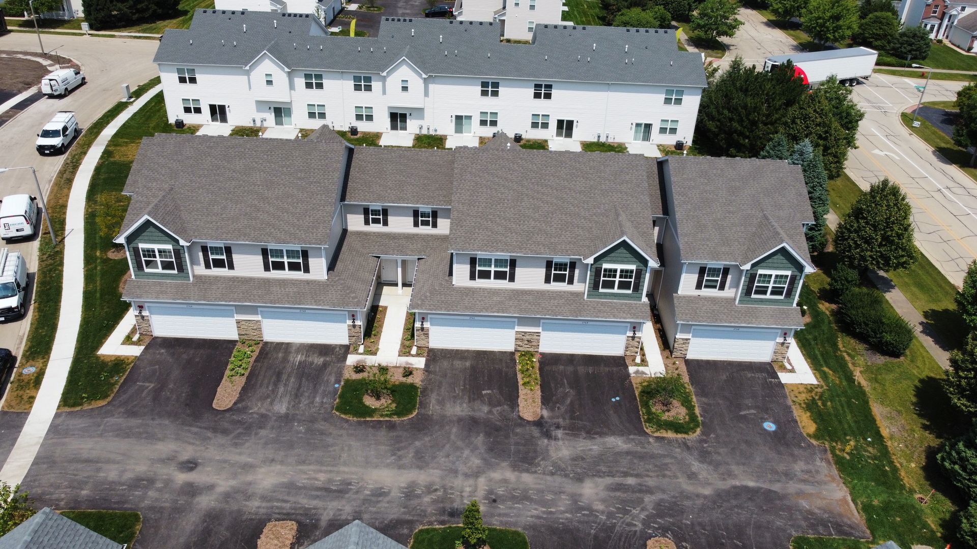 Aerial view of townhouse row with parked cars and a larger apartment building behind it.