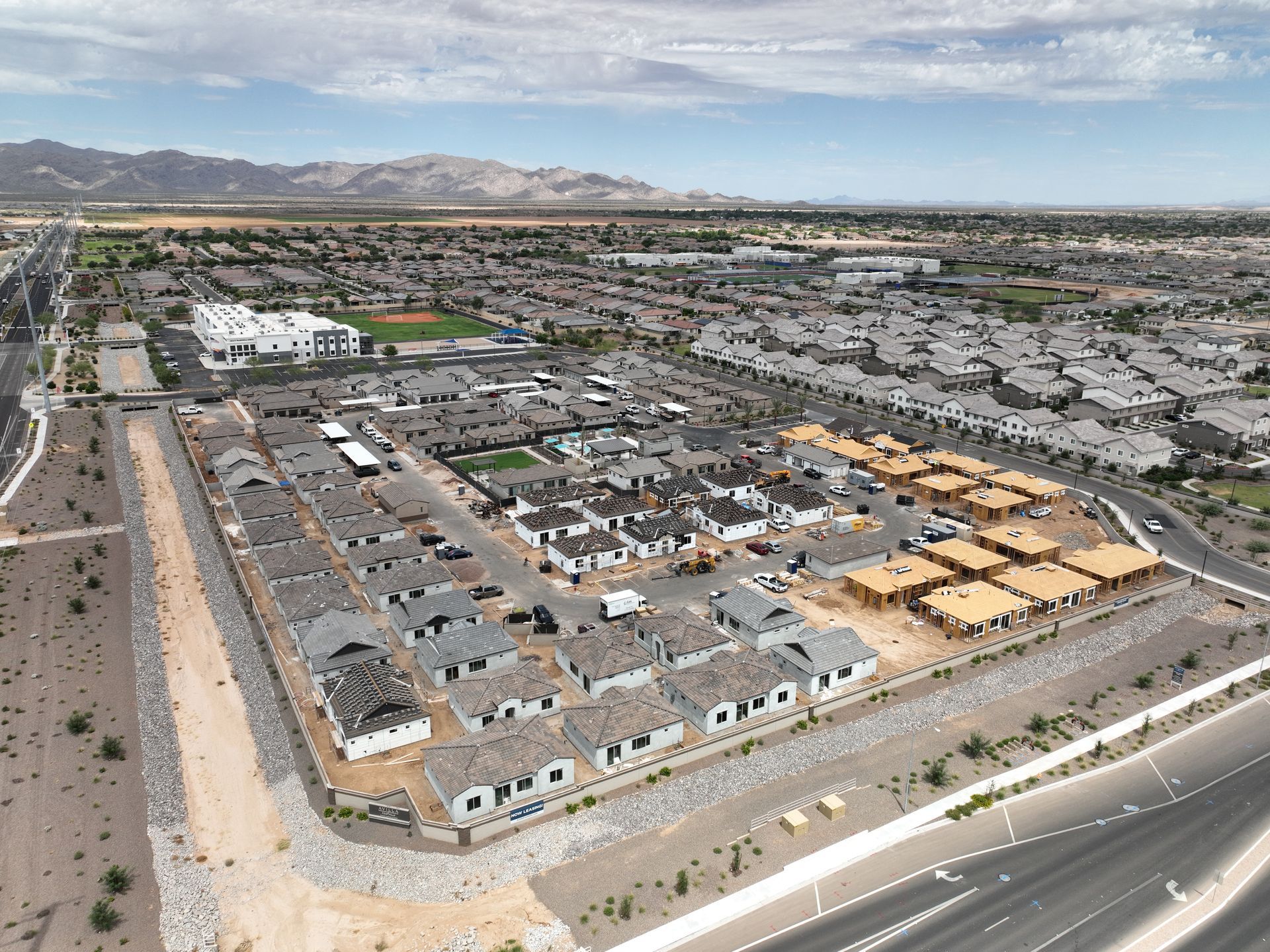 Aerial view of a large suburban housing development with roads, rooftops, and mountains in the background.