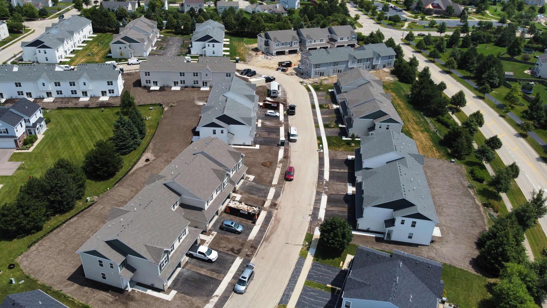 Aerial view of a suburban street with row houses, parked cars, and trees in a residential neighborhood