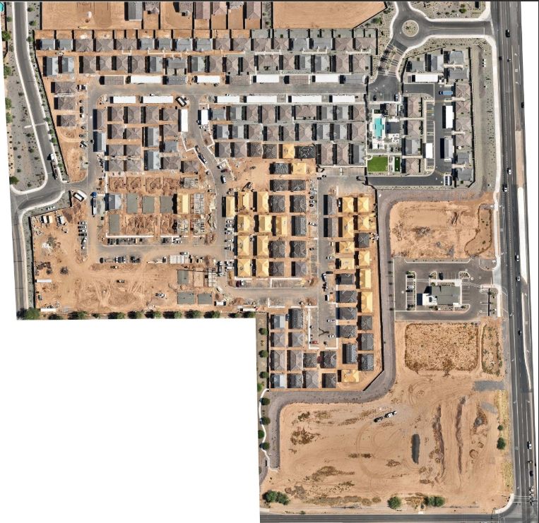 Aerial view of a desert apartment complex with rows of tan buildings, roads, and vacant lots.
