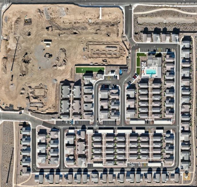 Aerial view of a residential neighborhood beside a large construction site, with rows of houses and roads.