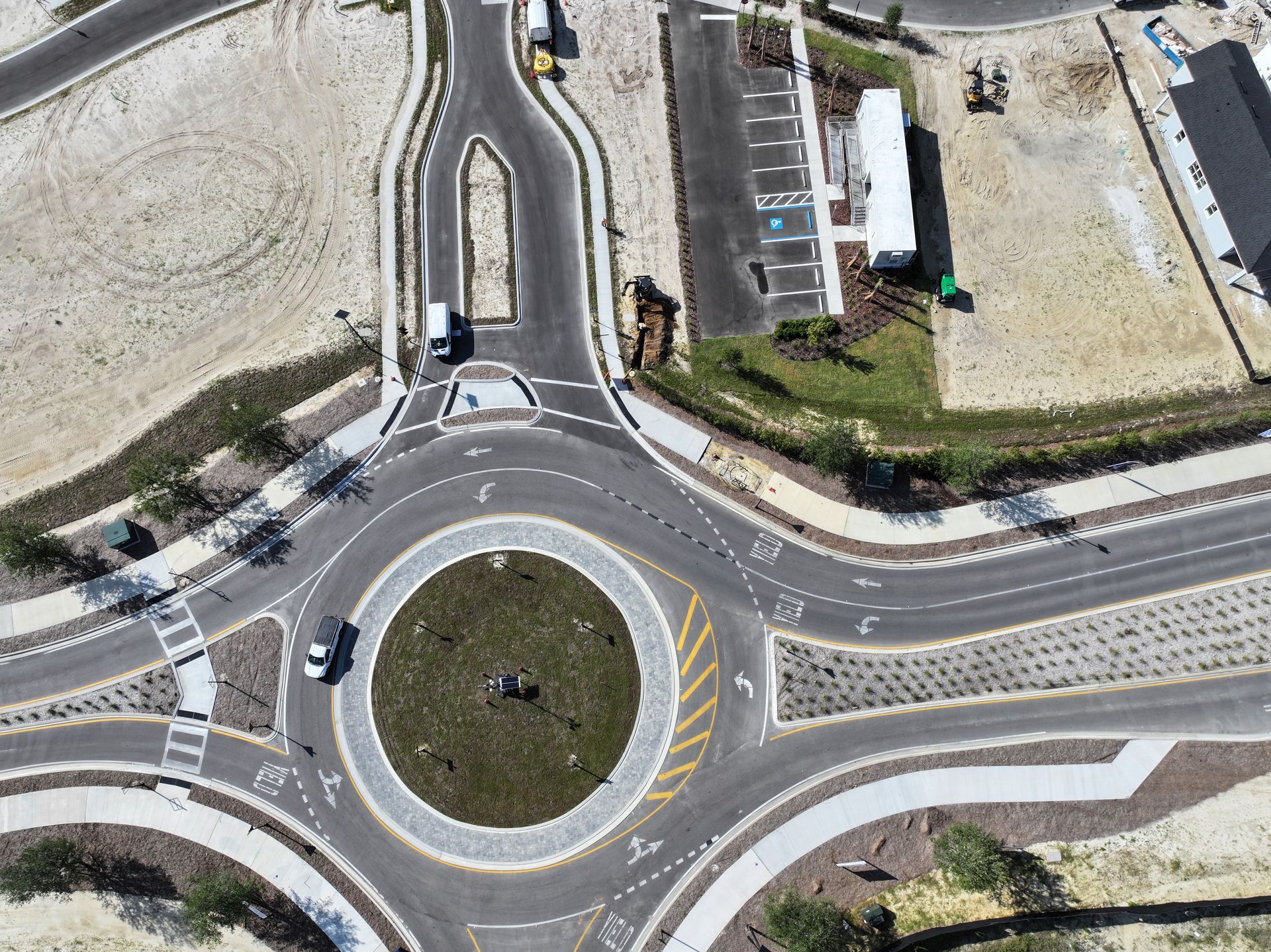 Aerial view of a roundabout with cars, roads, and surrounding buildings in a rural area