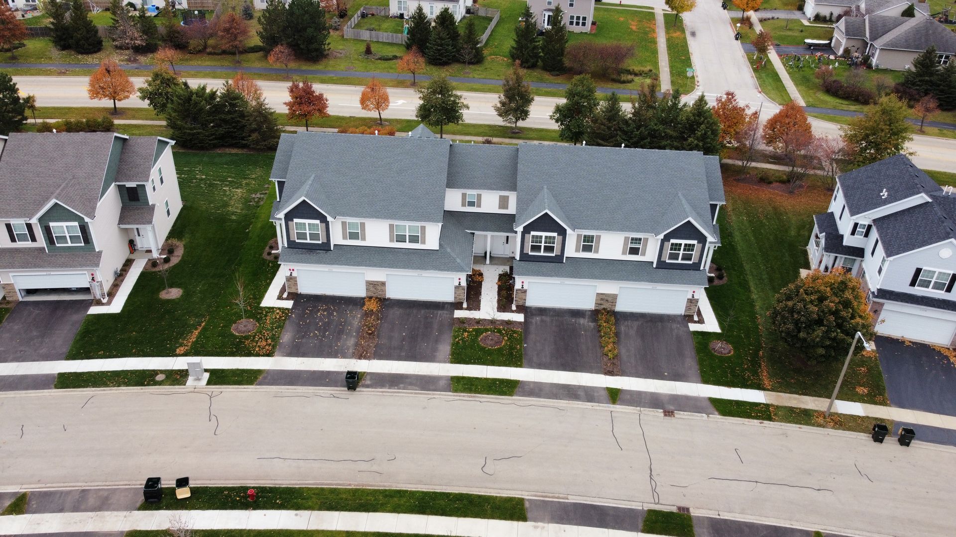 Aerial view of three suburban houses with driveways and a tree-lined street in front
