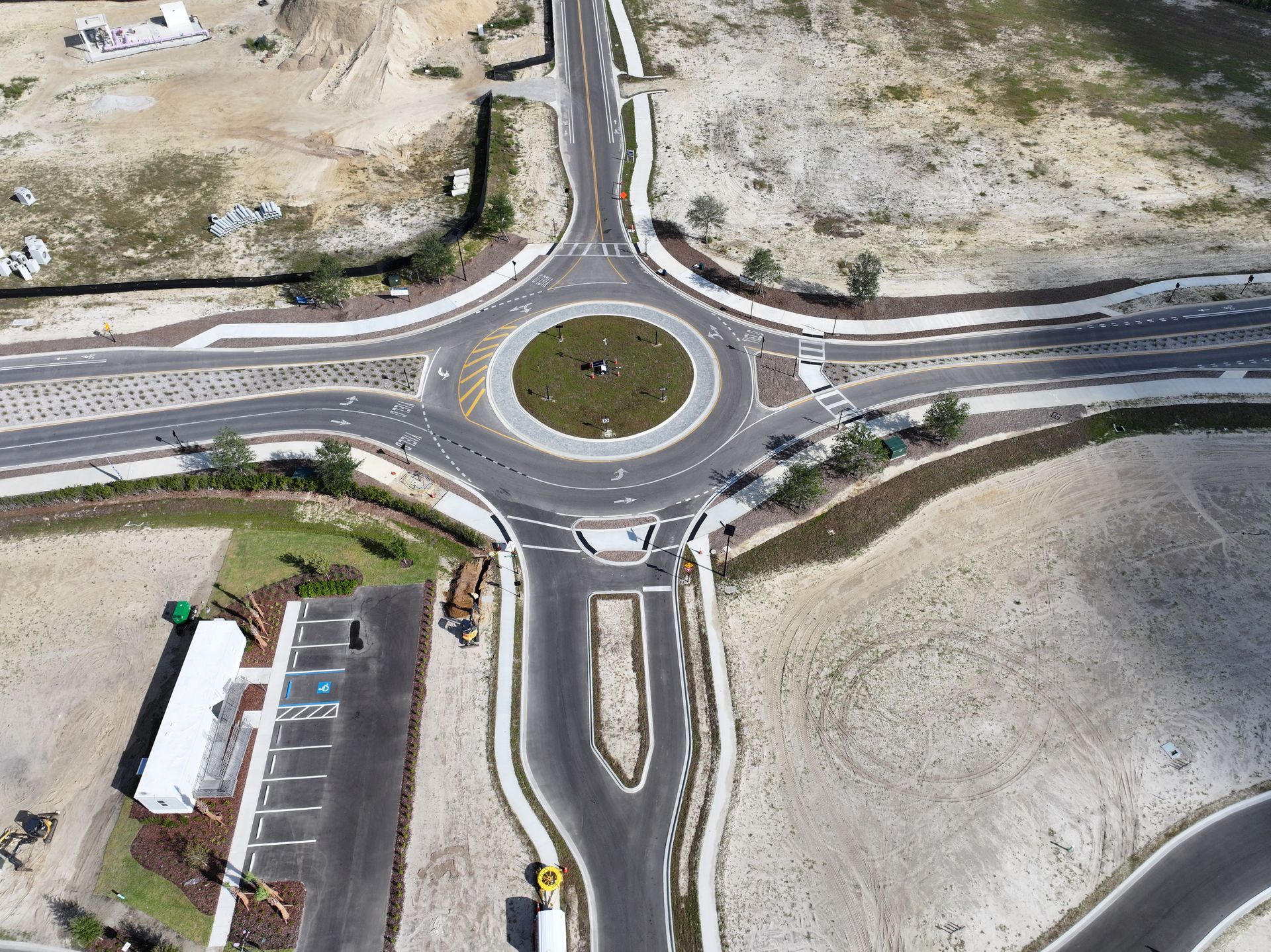 Aerial view of a roundabout with four roads, bordered by dry open land and a small building.