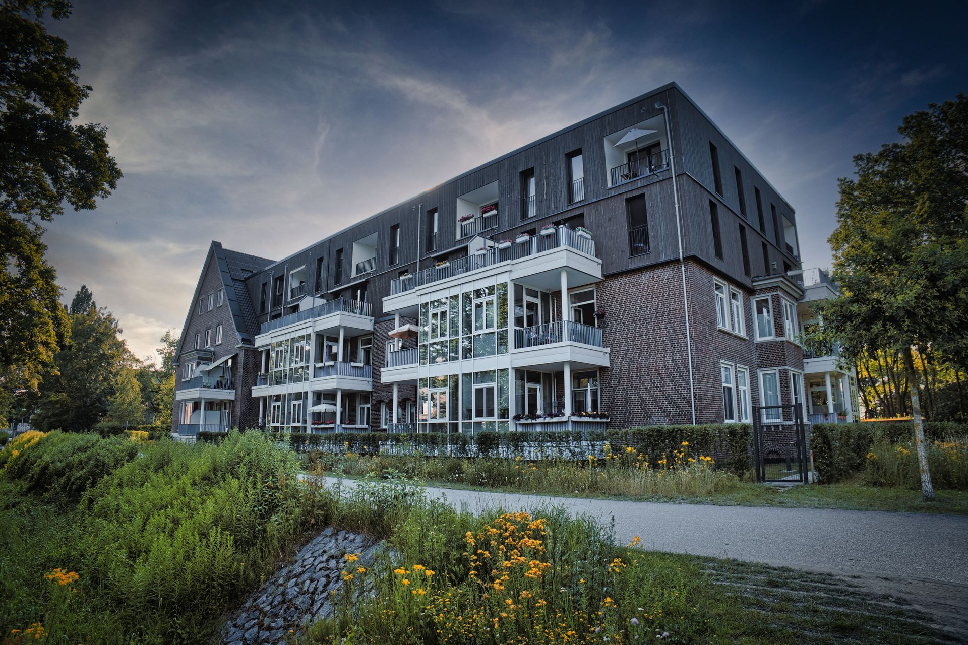 Modern apartment building with balconies, surrounded by greenery under a cloudy sky