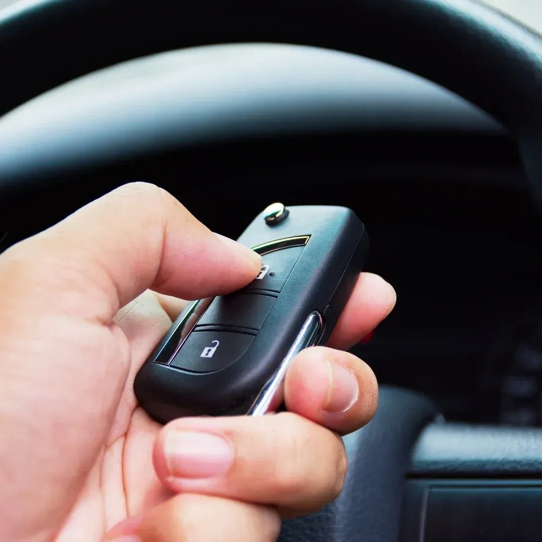 Hand holding a black car key fob in front of a steering wheel Hand holding a black car key fob in front of a steering wheel