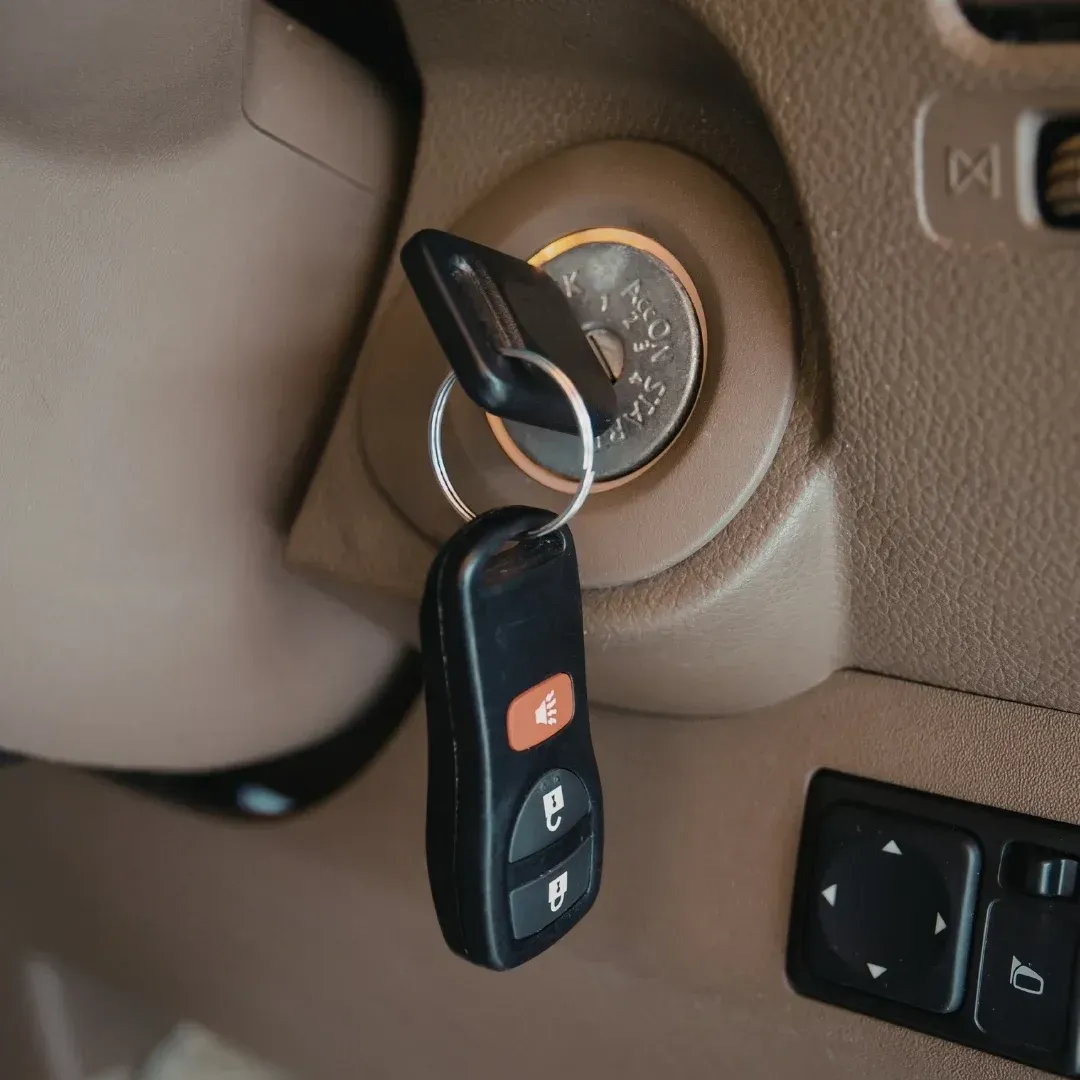 Car key in ignition beside a black remote key fob hanging from the steering column Car key in ignition beside a black remote key fob hanging from the steering column