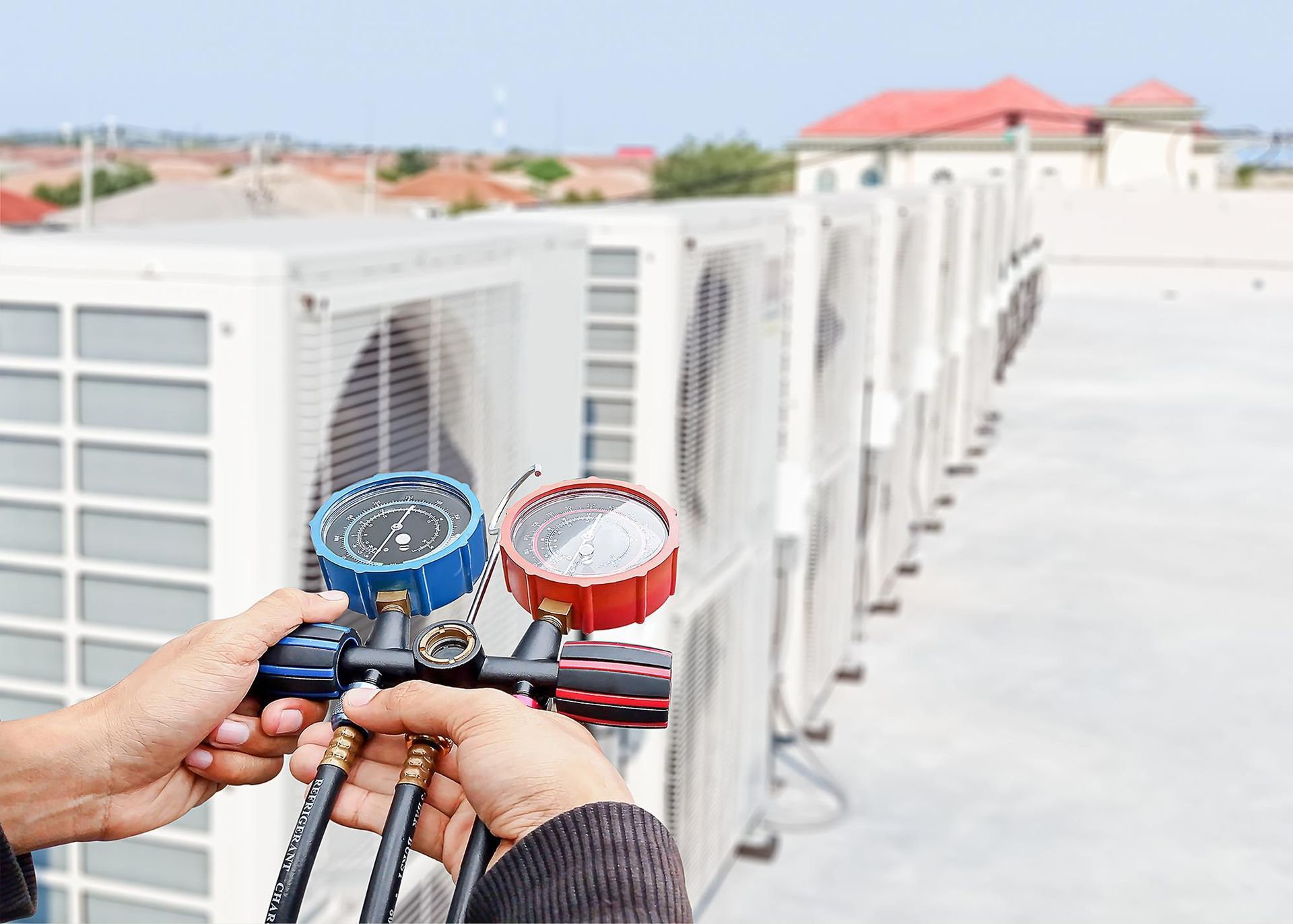 Hands holding HVAC pressure gauges on rooftop air-conditioning units