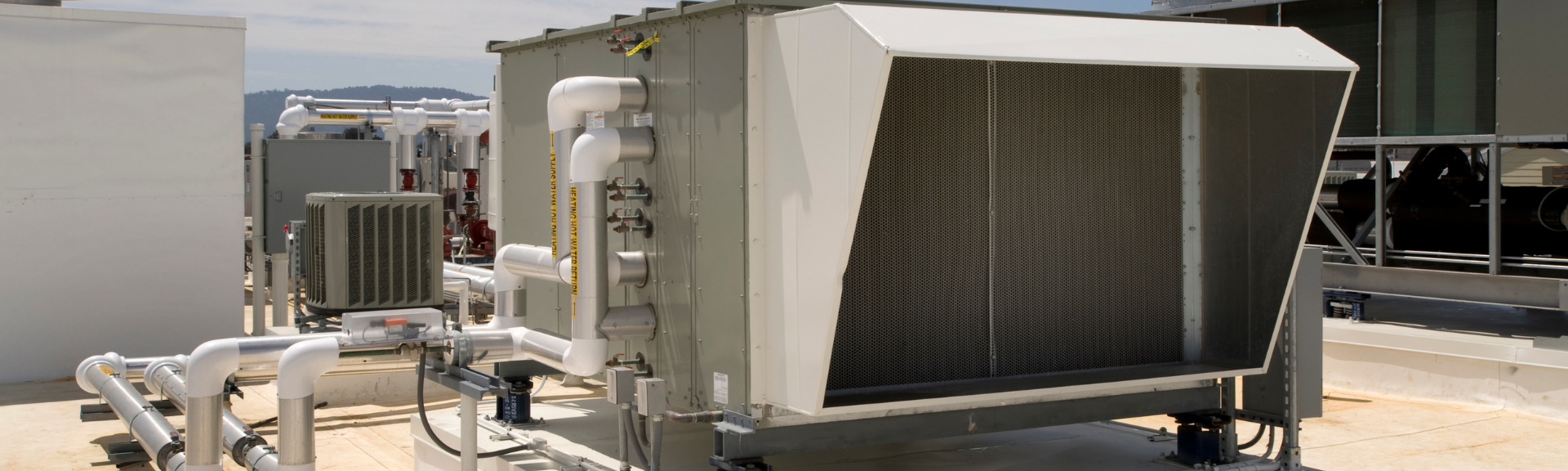 Industrial HVAC unit on a rooftop, with metal vents and ductwork in bright sunlight