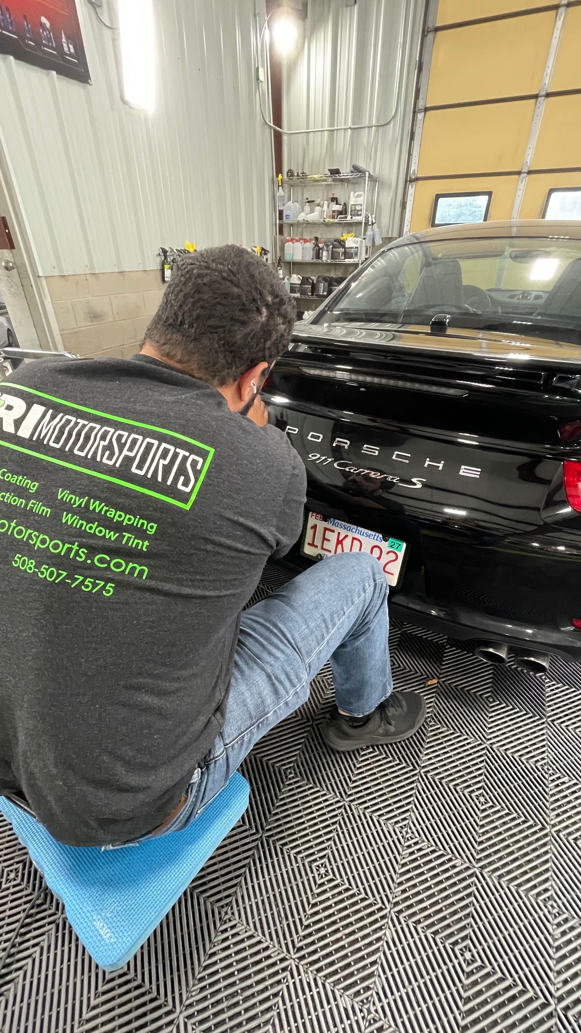 A man is kneeling down in front of a black car.