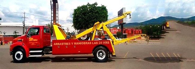 Una grúa roja con una grúa amarilla en la parte trasera está estacionada al costado de la carretera.