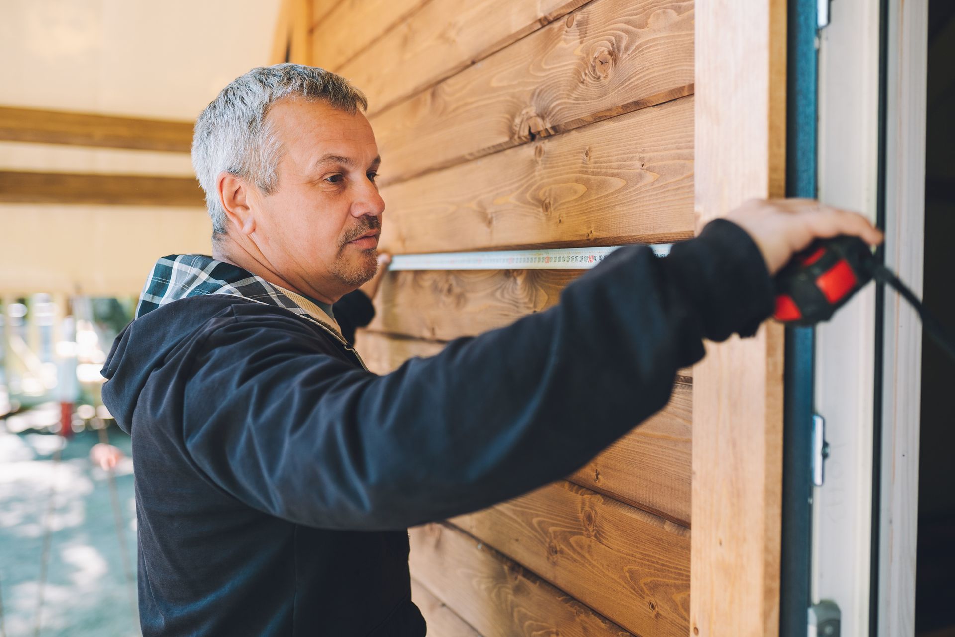 Builder using a tape measure to assess a wooden house.