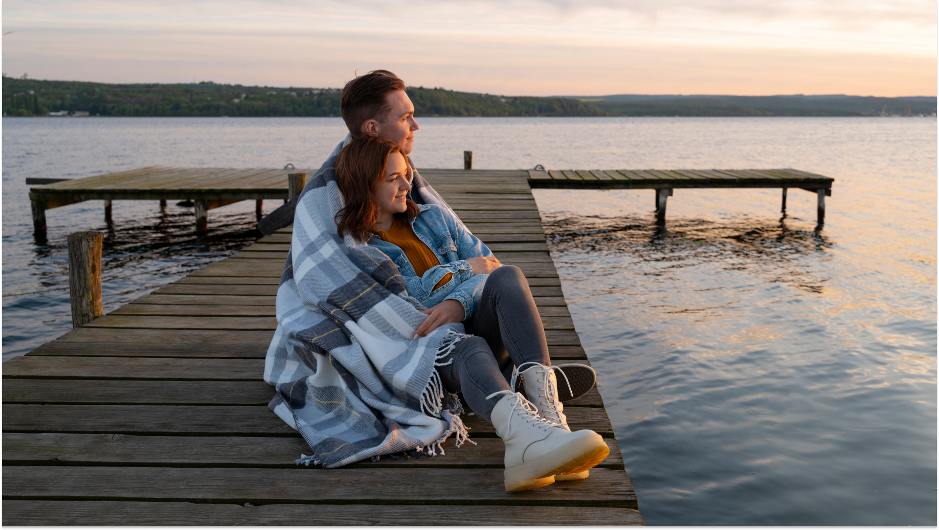 couple sitting on boardwalk looking at lake cuddling