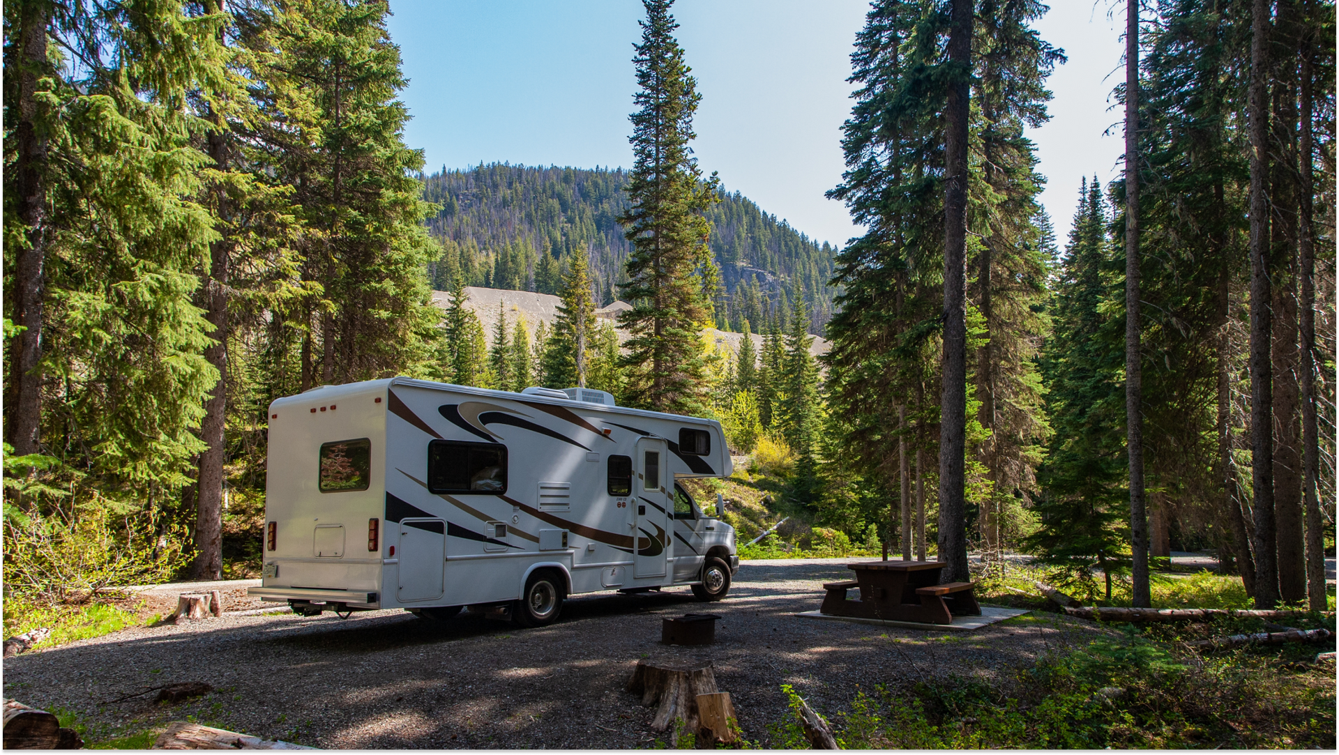 white RV in the shade in the woods on a road
